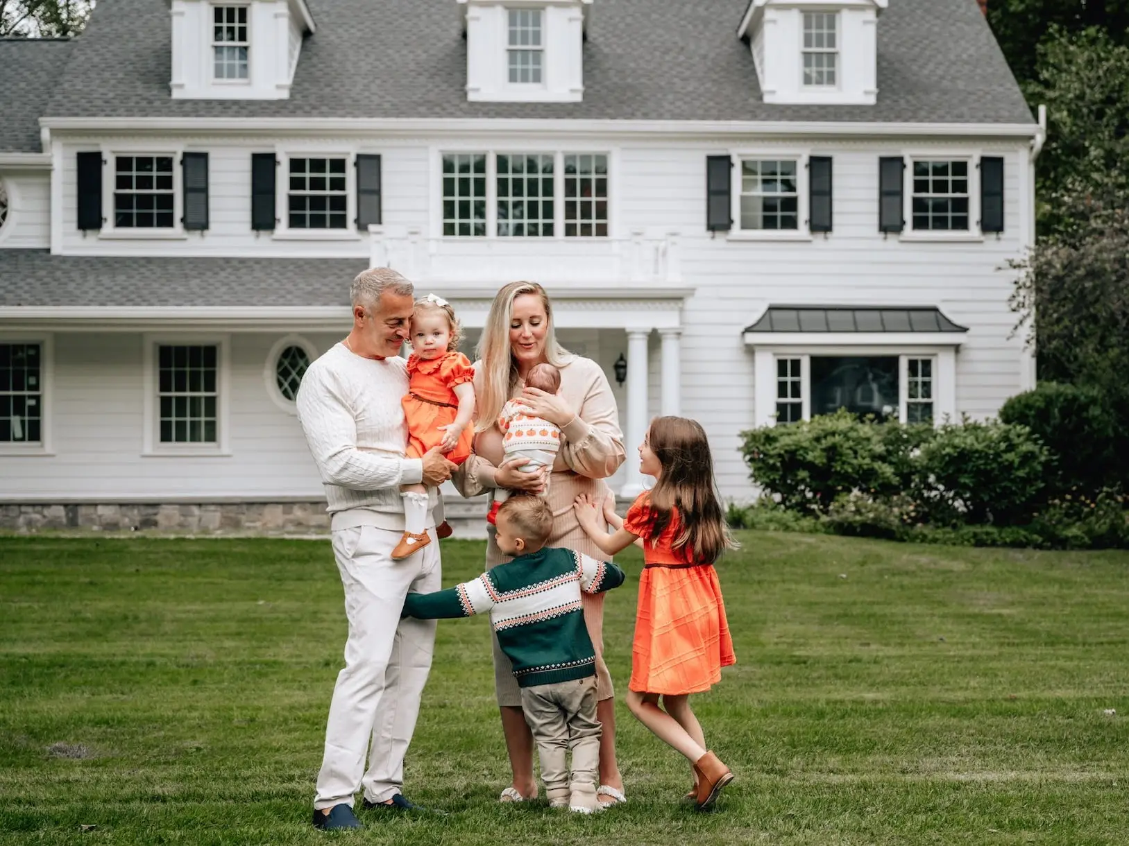 A family of five hugs in front of their white house.