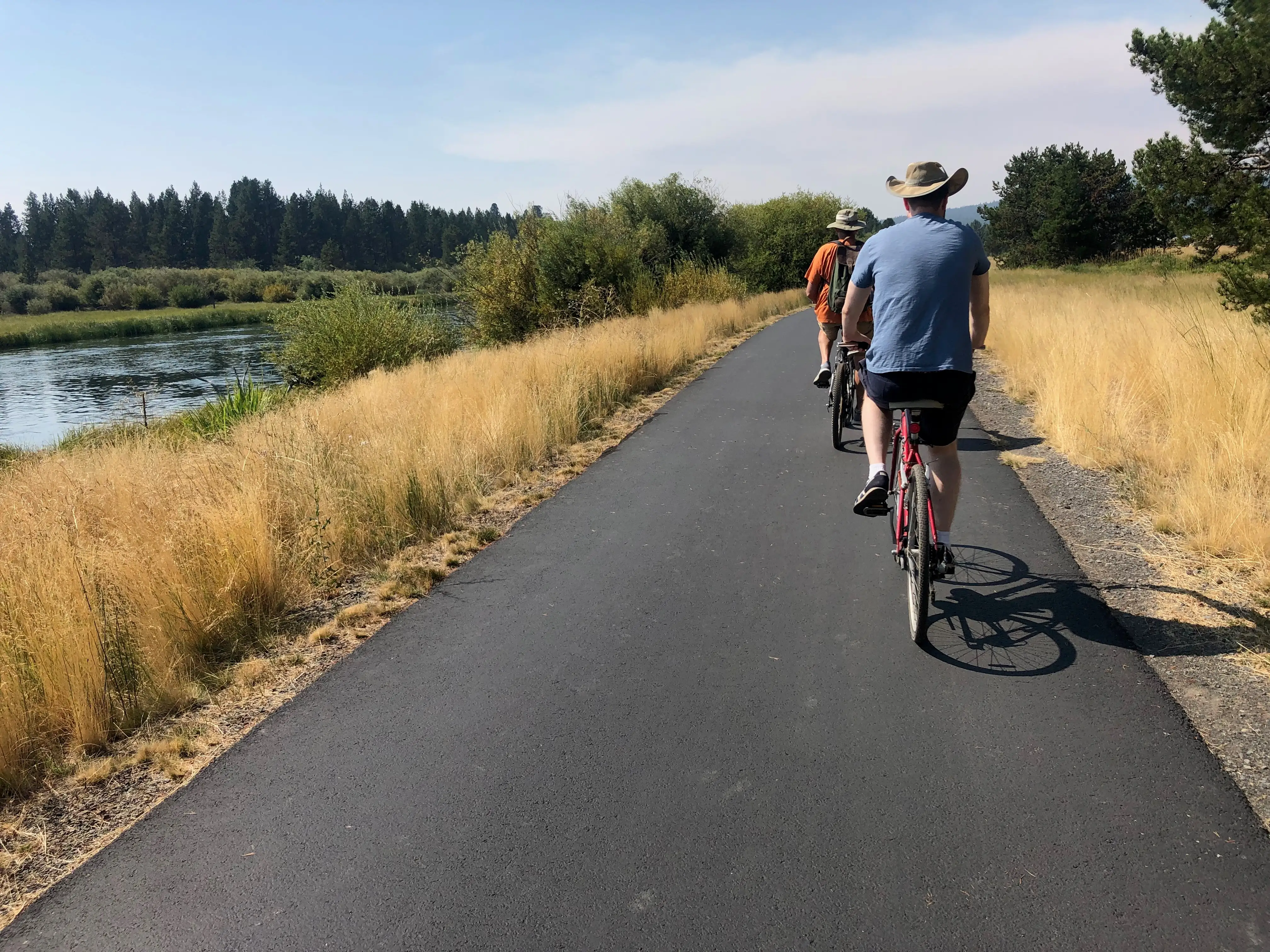 People riding bikes on pathway next to water in Bend