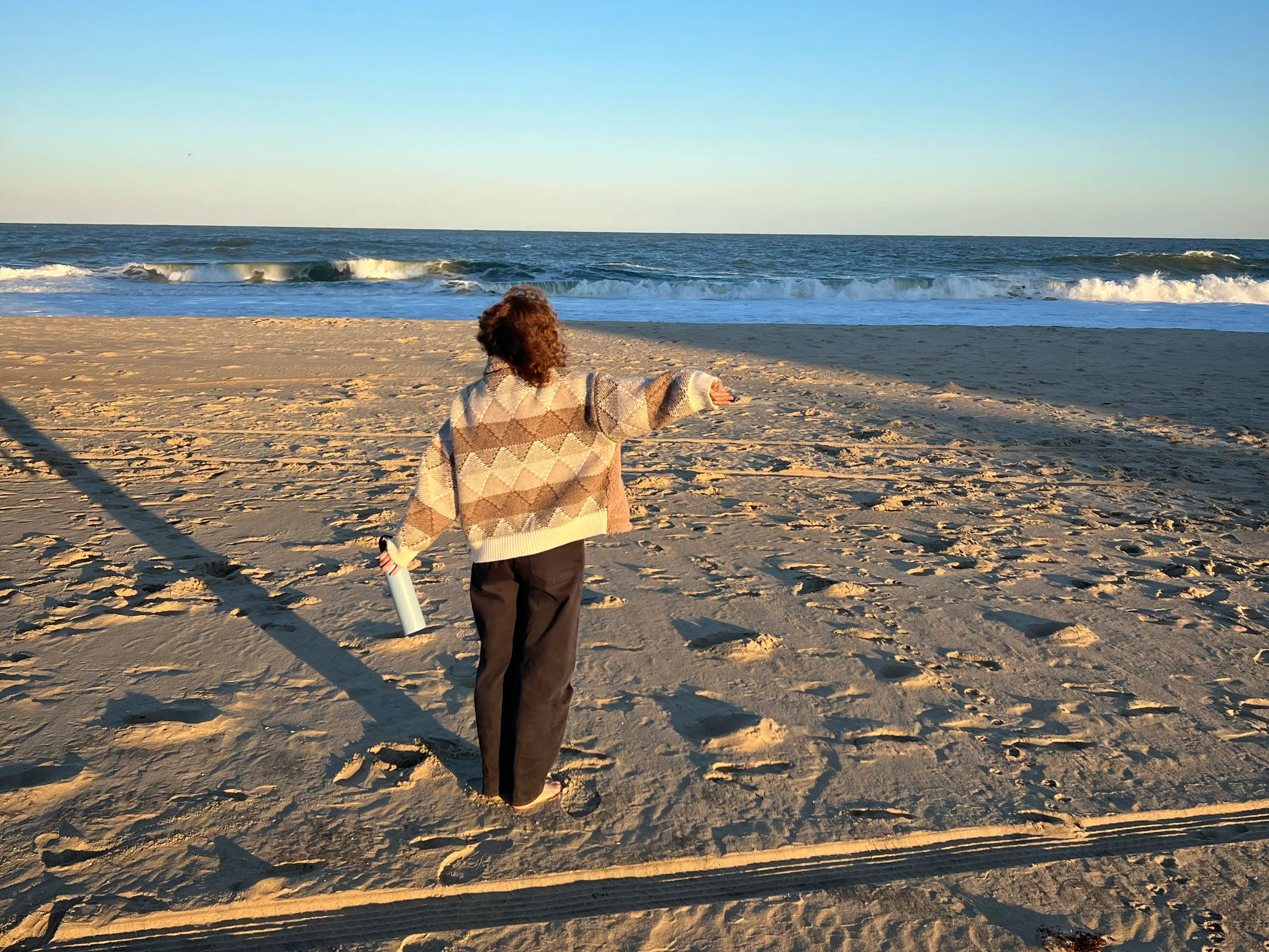 Haley stands in a coat with her arms stretched out, looking out at the ocean.