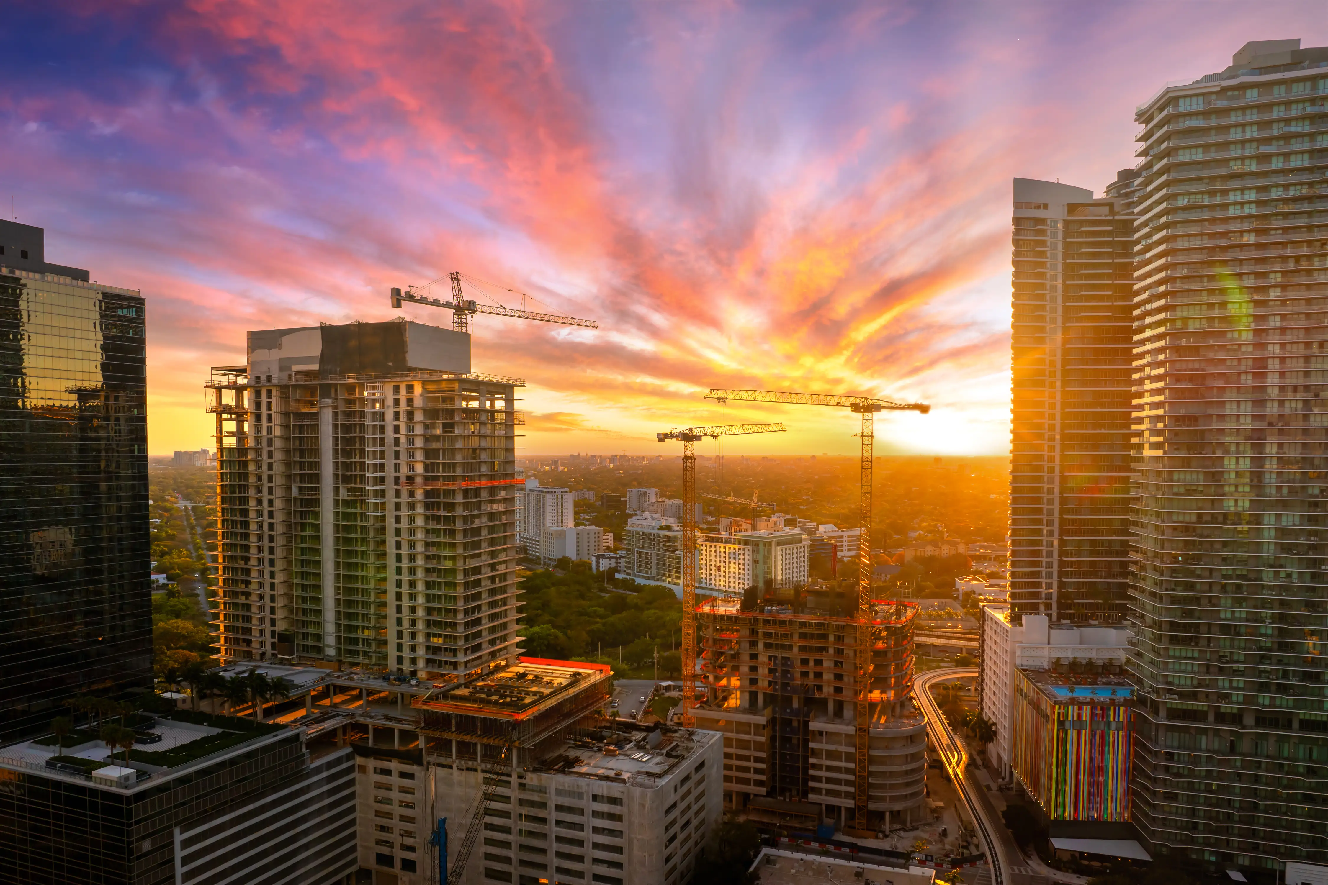 A sunset over buildings in Miami, Florida, with cranes over new high-rise buildings under construction.