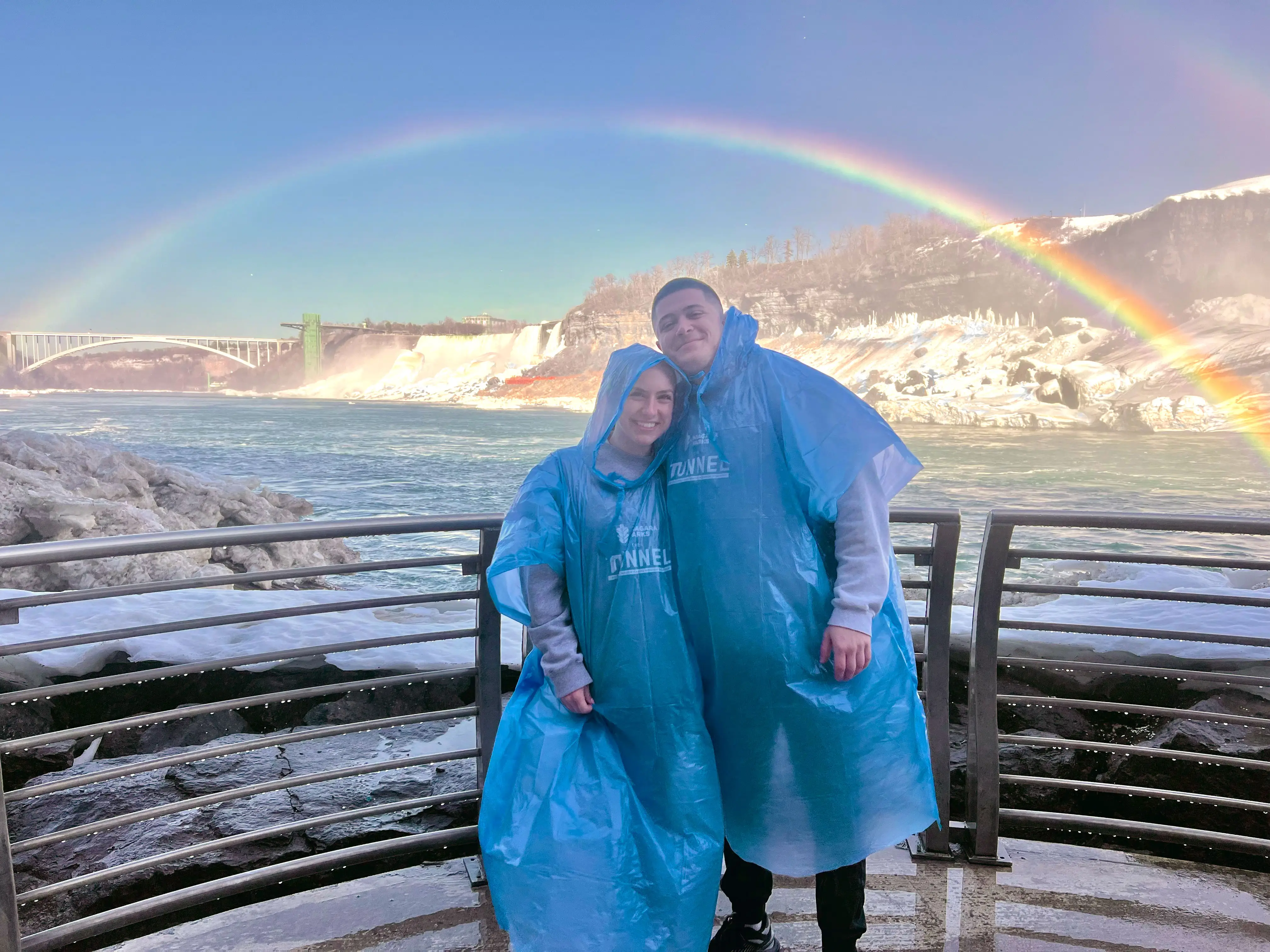 Amanda and her boyfriend pose in ponchos under a rainbow at Niagara Falls.