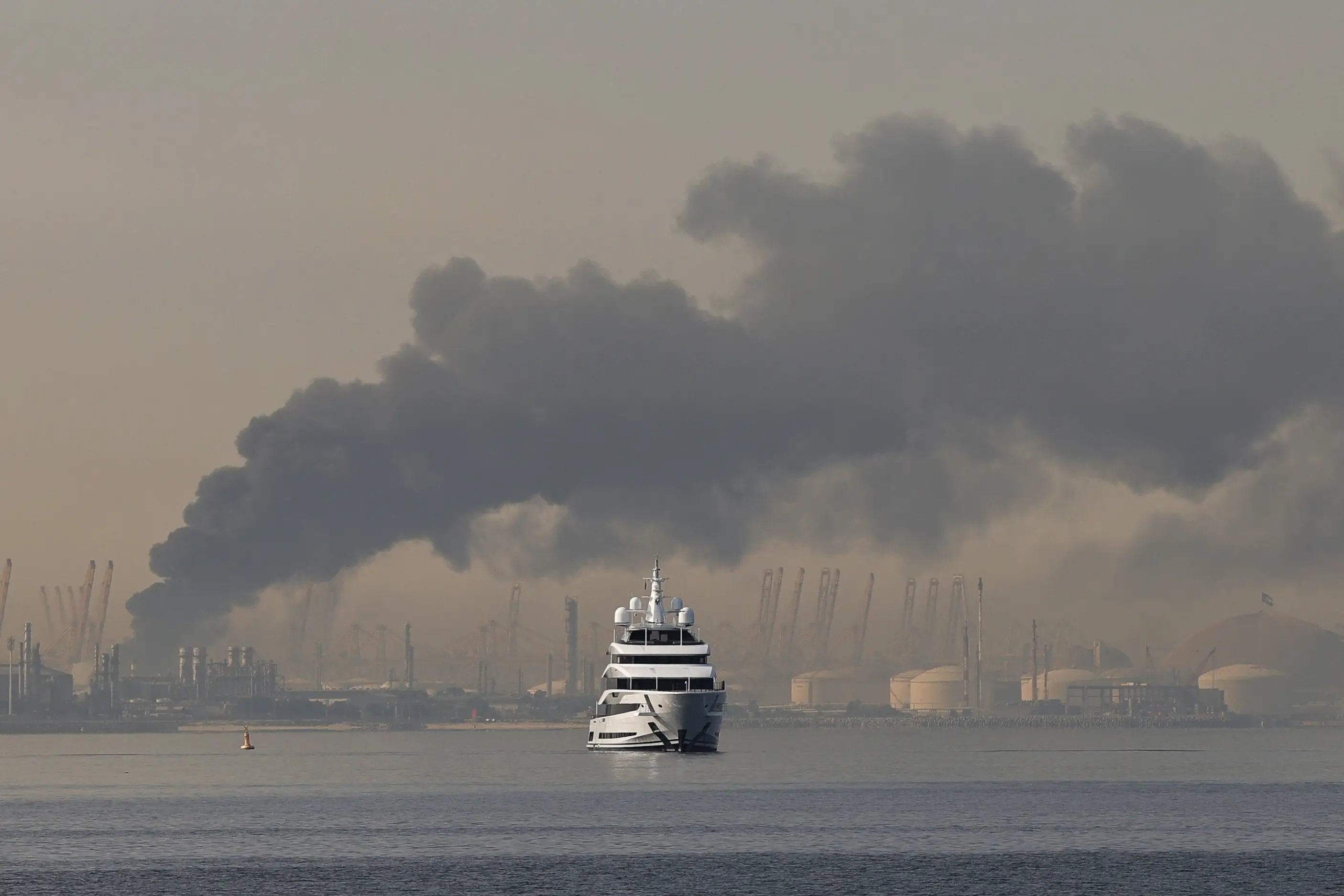 A yacht sails past a plume of smoke rising from the port of Jebel Ali