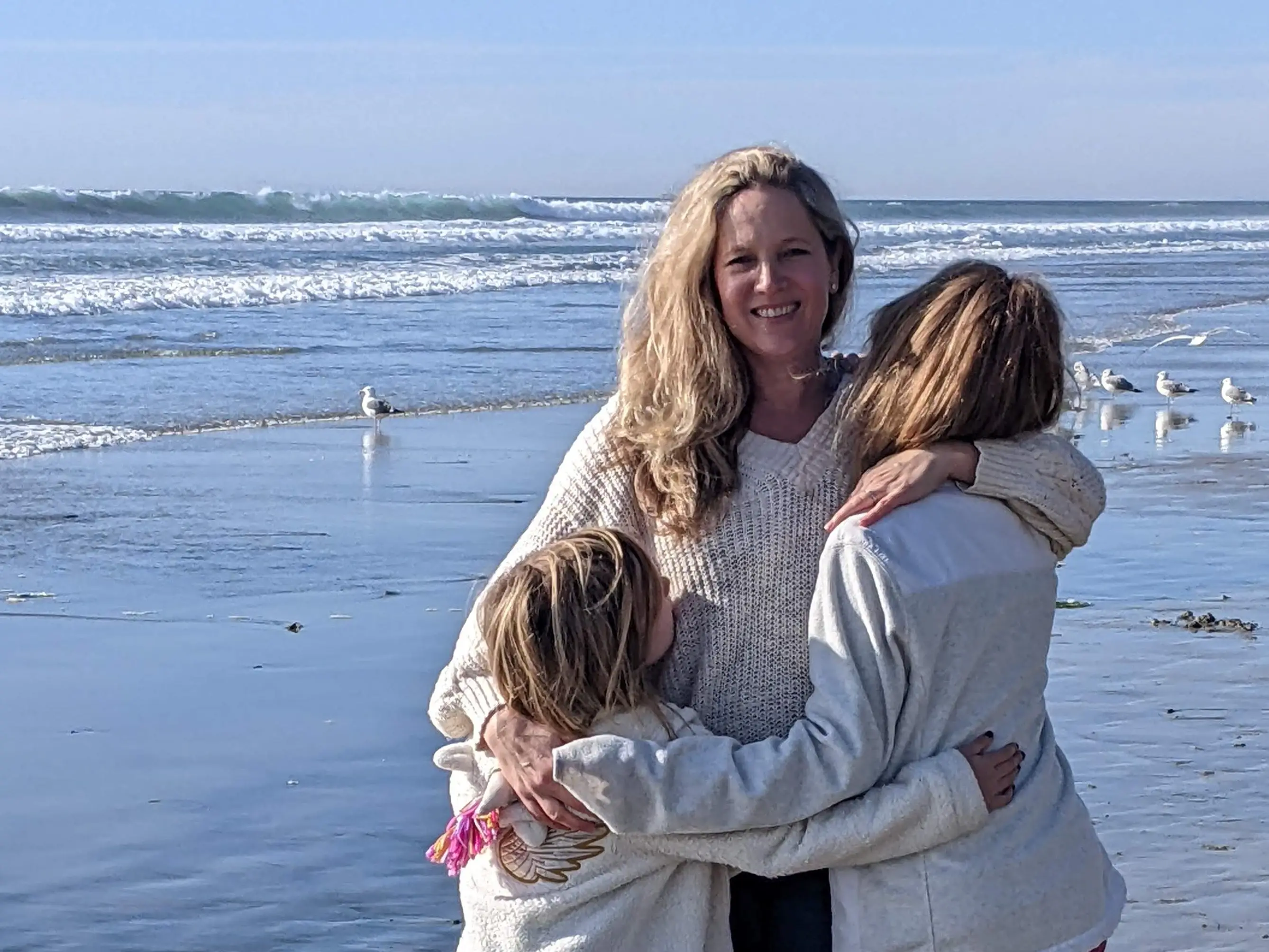 Woman with two daughters with the ocean and seagulls in the background.