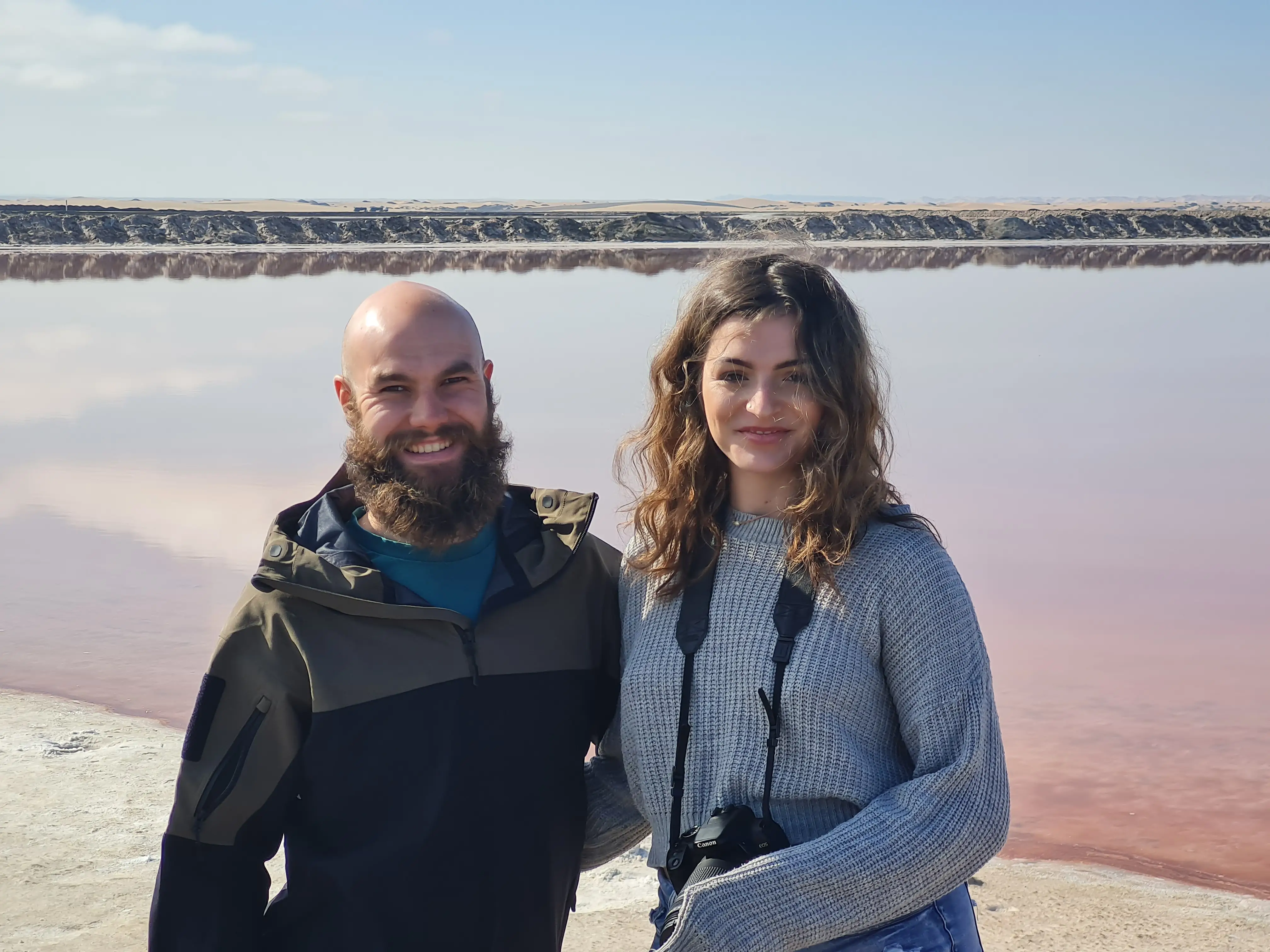 Man and woman smiling in front of body of water outside