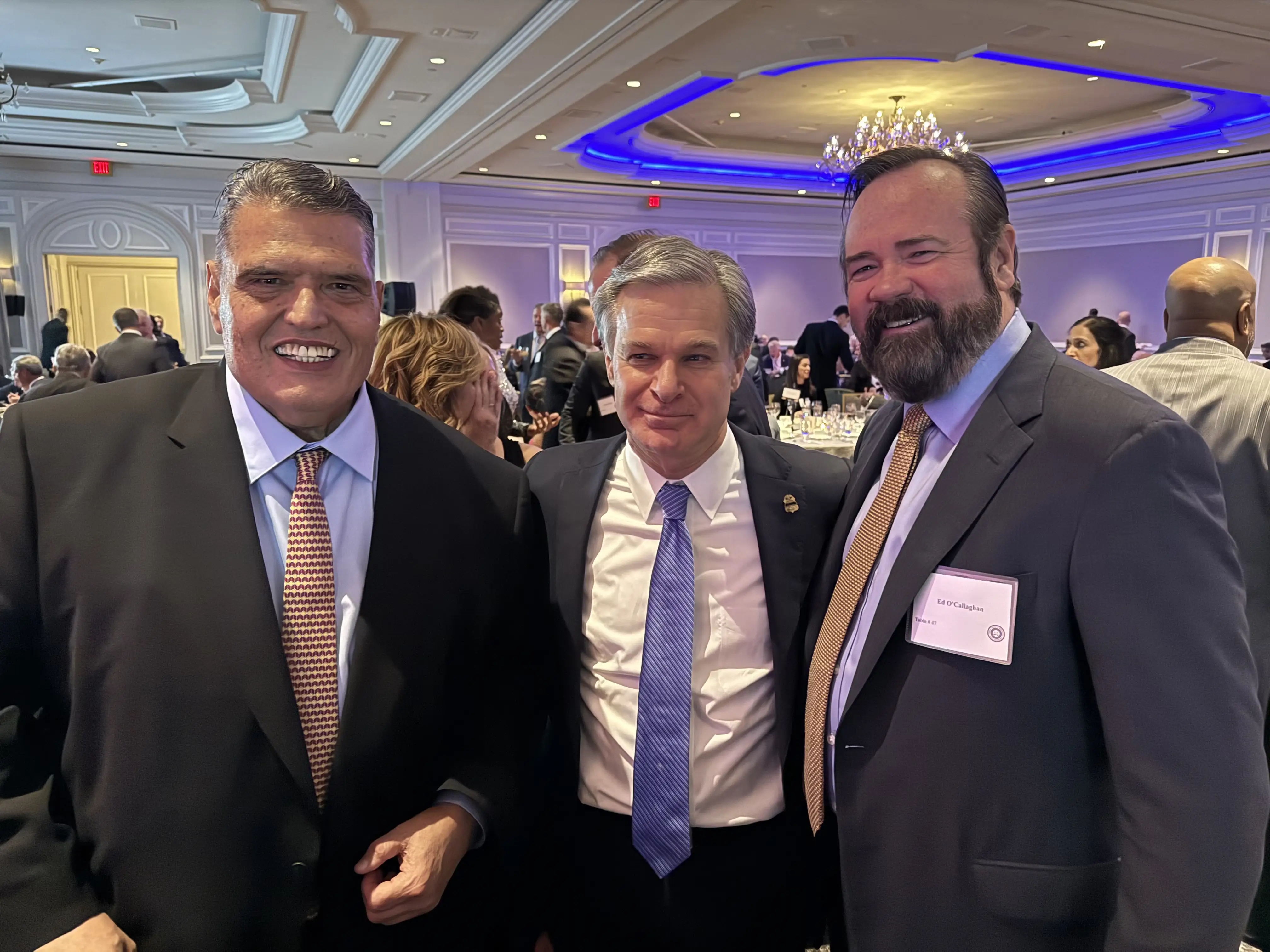 Three men in suits in a crowd at an event.