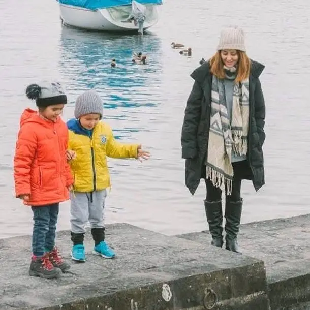 Kids standing on stones next to woman near water