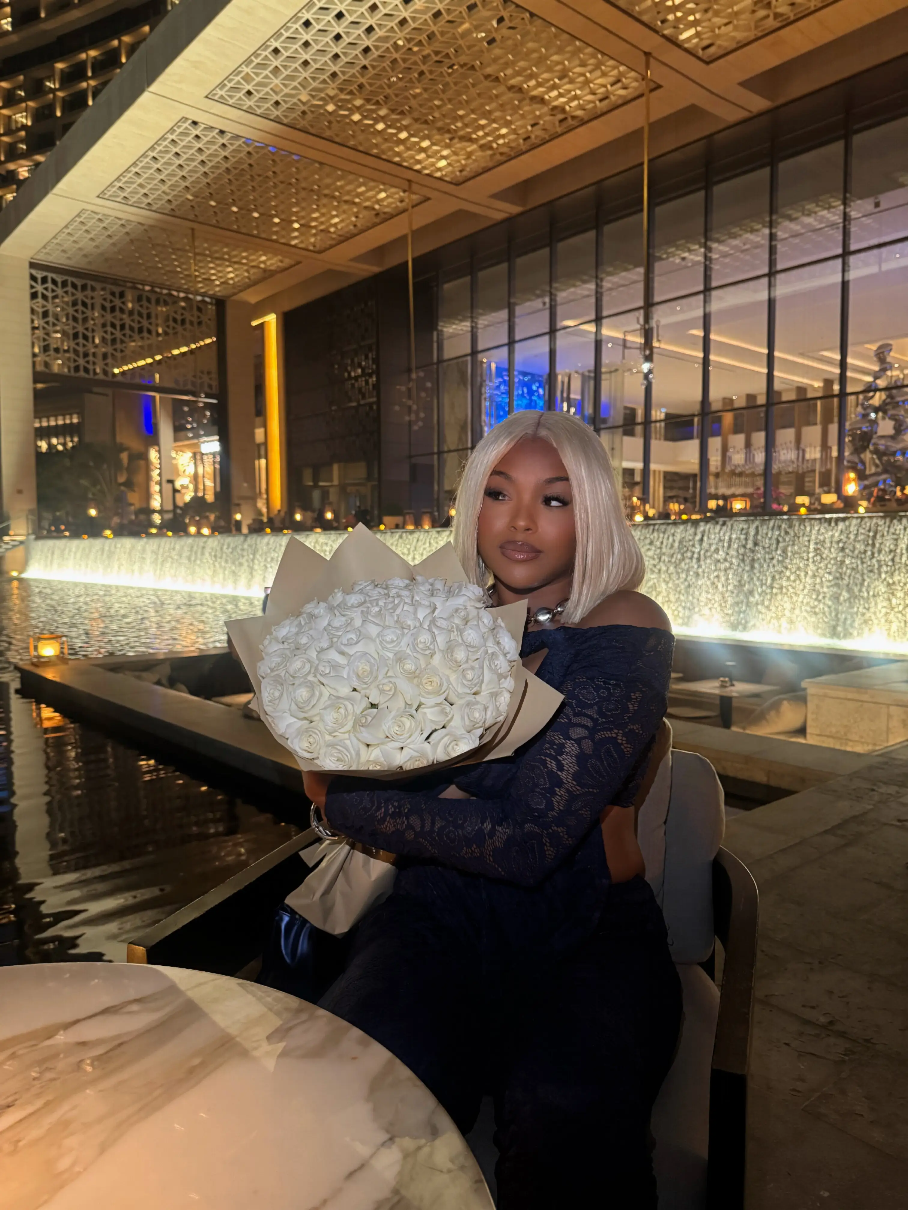 Young lady dressed in black, seated and holding a bouquet of white roses.