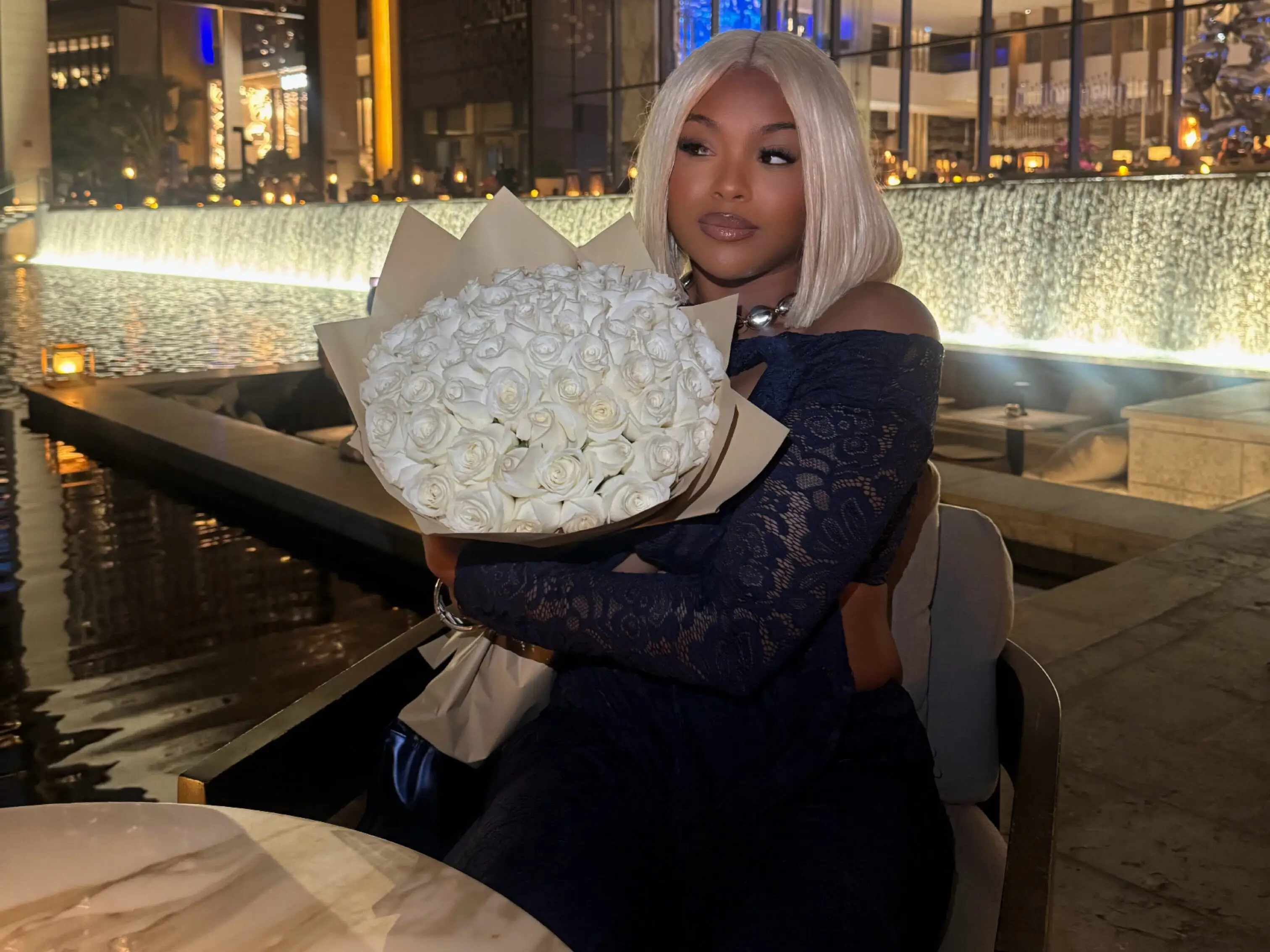 Young lady dressed in black, seated and holding a bouquet of white roses.