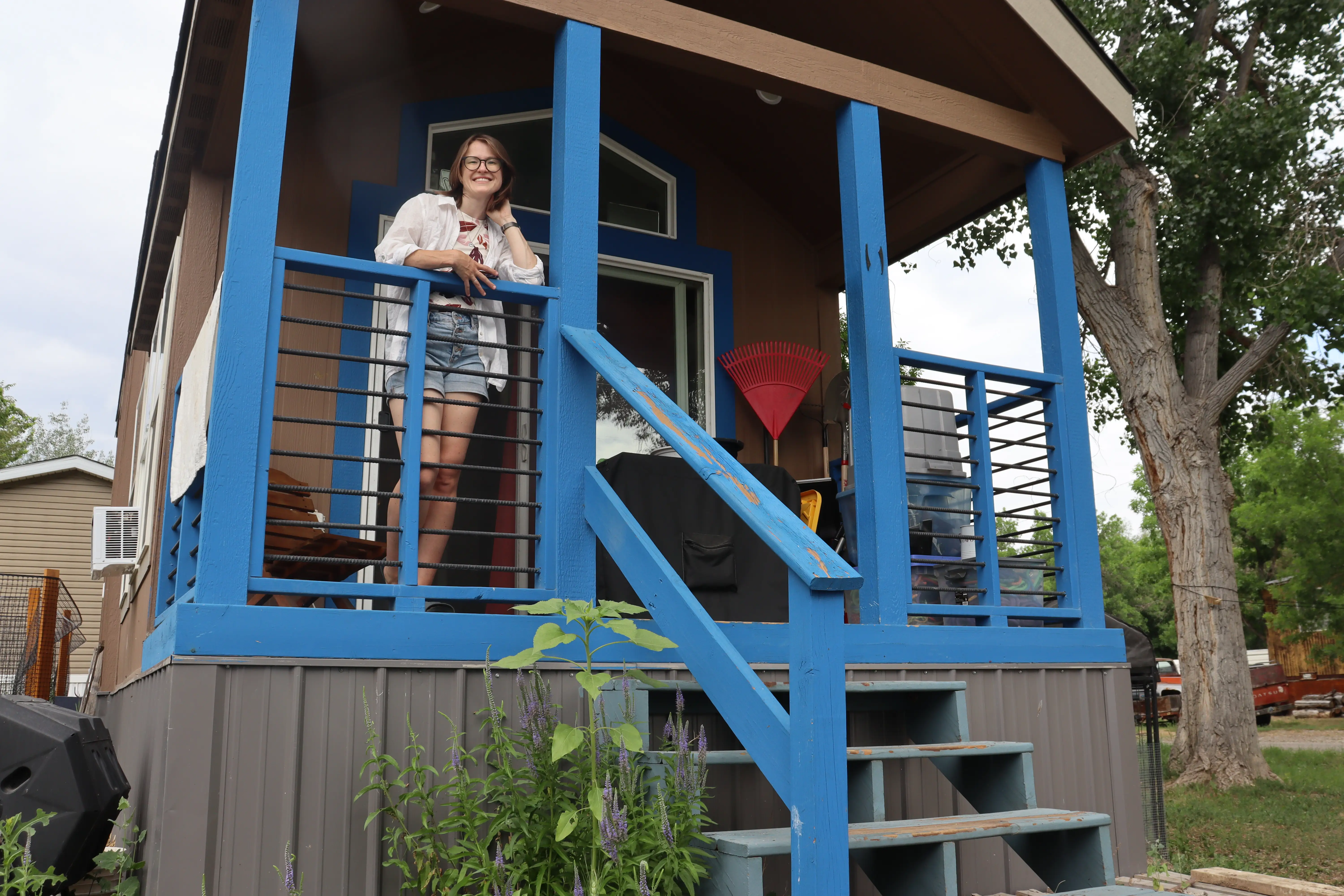 Woman smiling from porch of blue-painted railing on tiny home porch