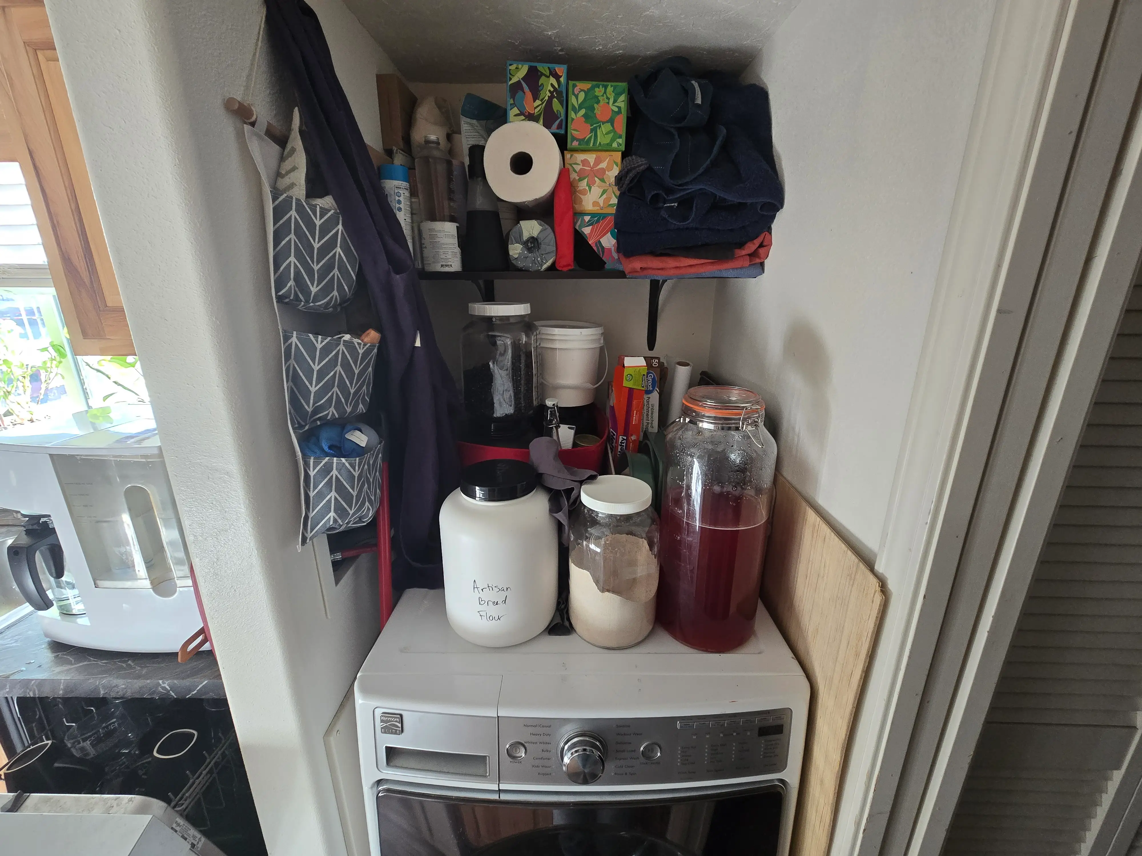 washing machine with detergent on top of it and shelf with paper goods above it in alcove