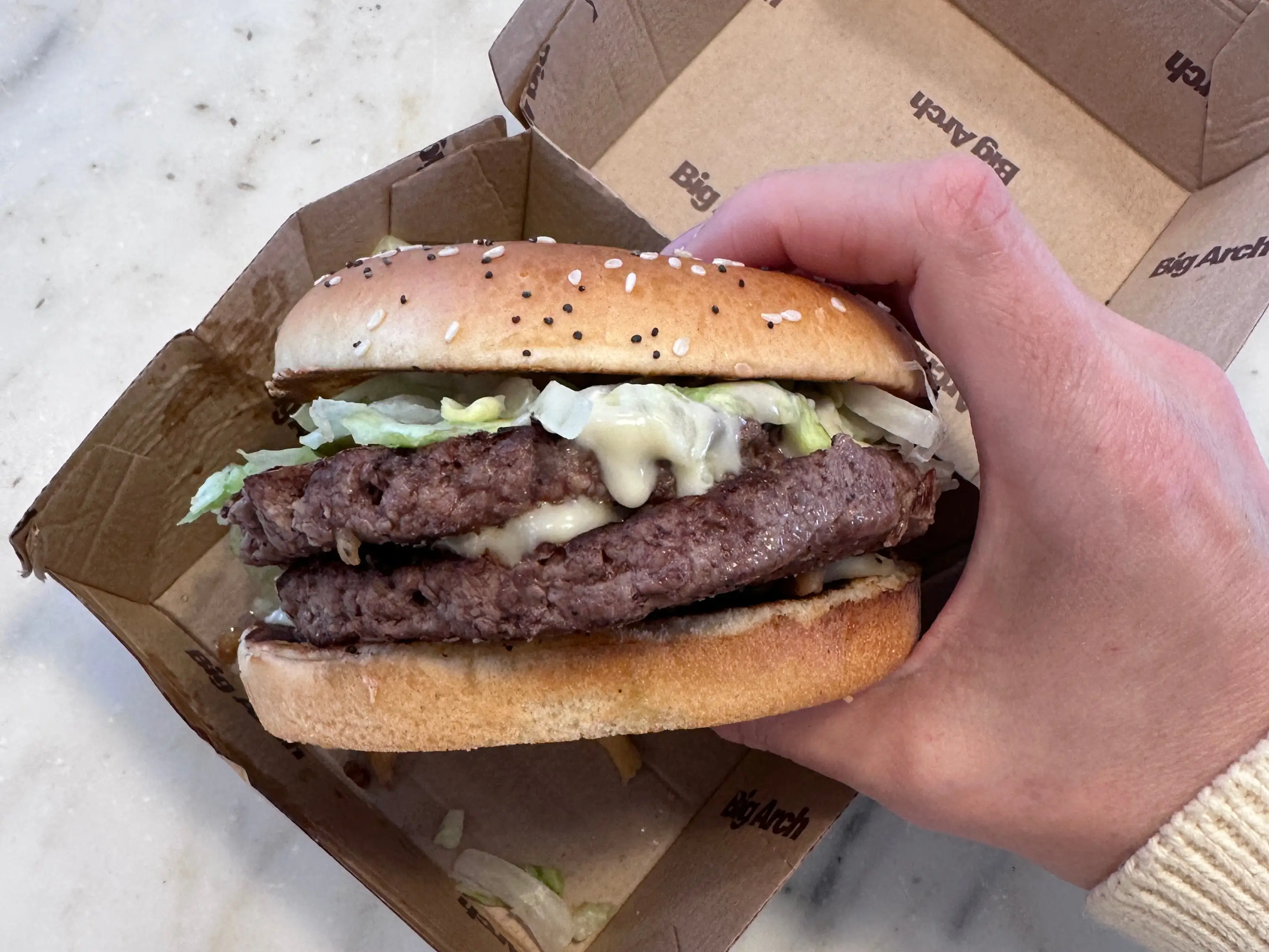 a hand holding a mcdonalds big arc burger