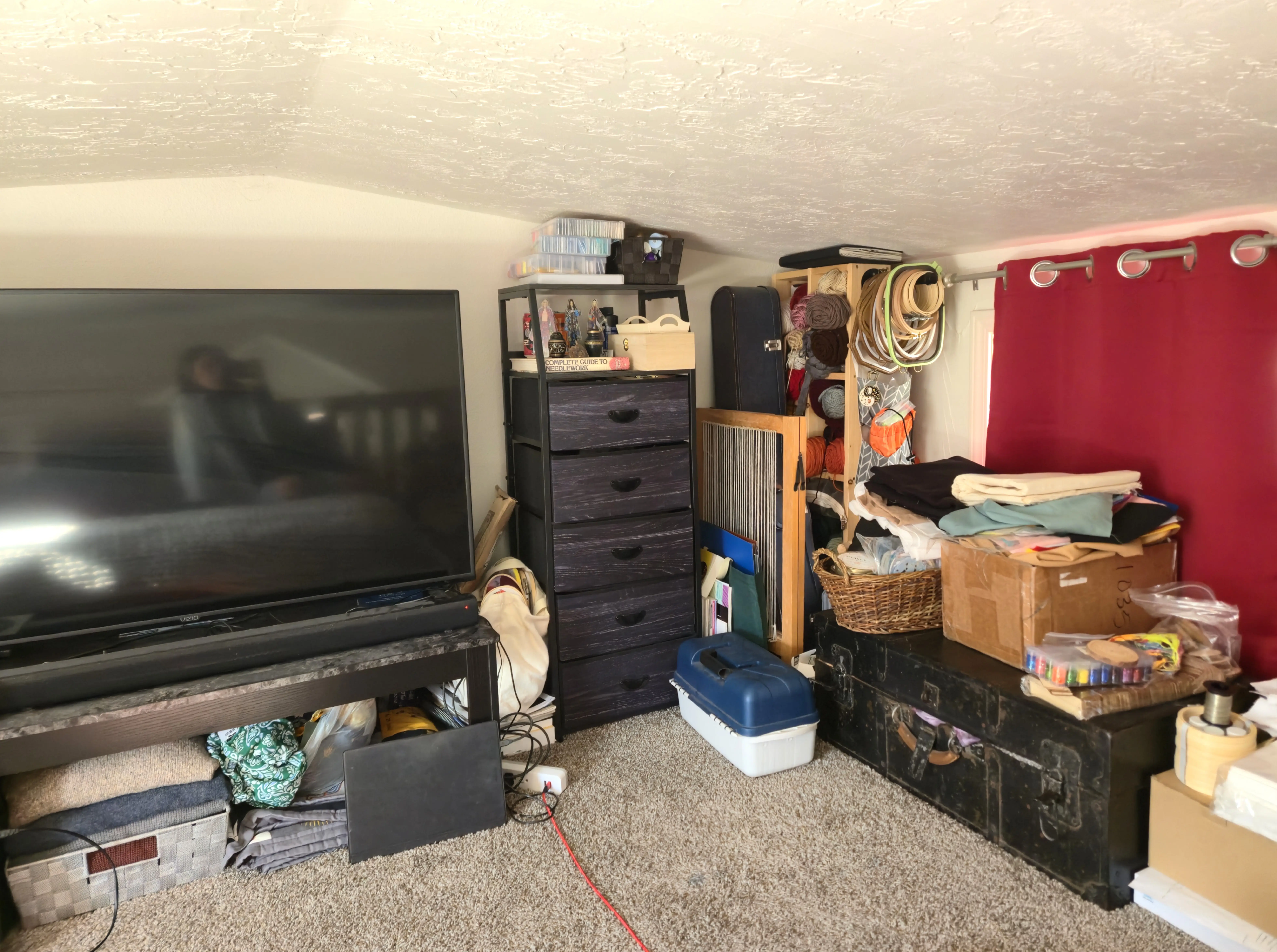 TV with bins below it next to dresser, shelving unit, vintage trunk with boxes and craft supplies on top of it