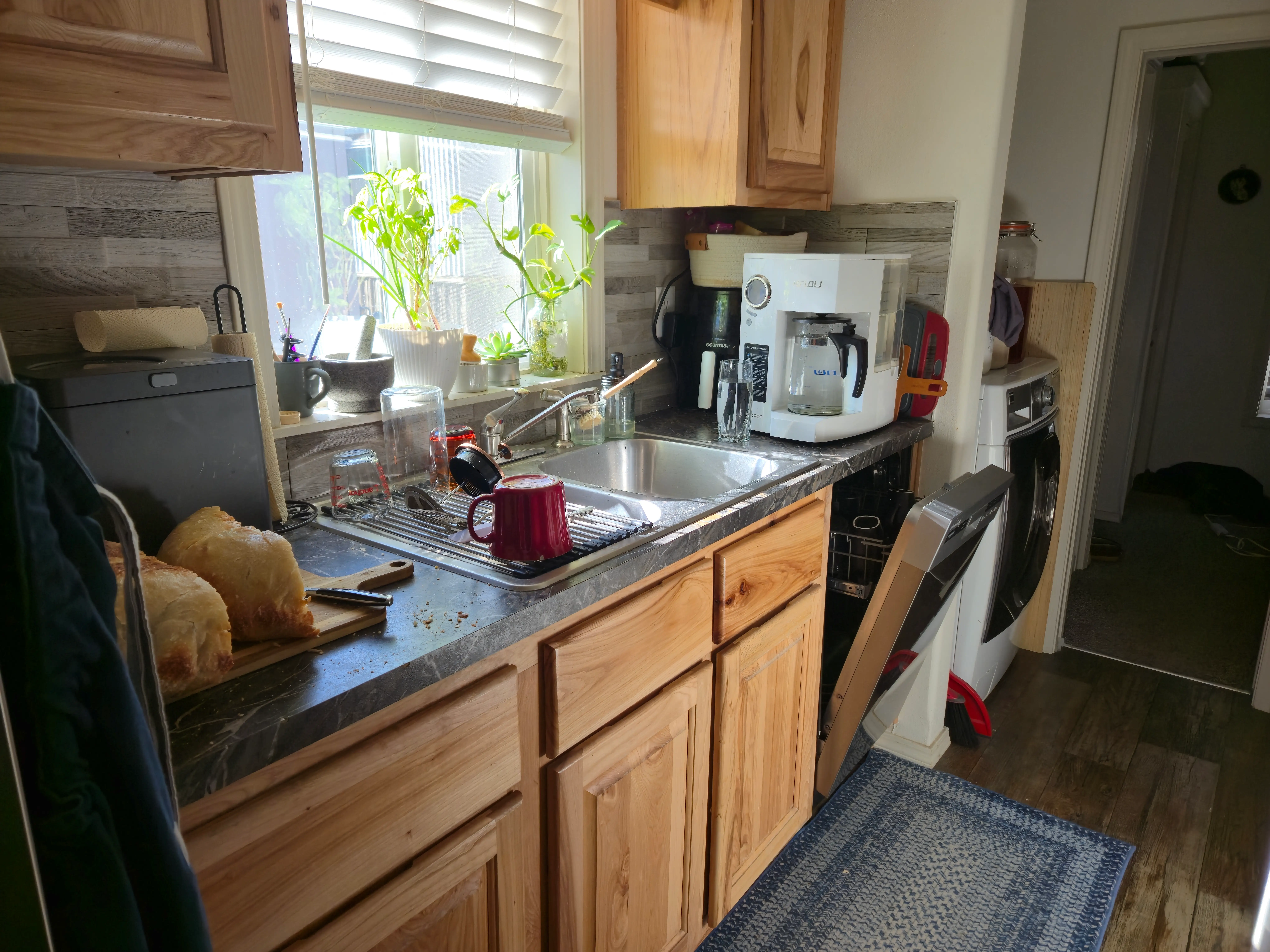 View of kitchen countertops with coffee maker, dishwasher, window above sink, and washing machine next to dishwasher