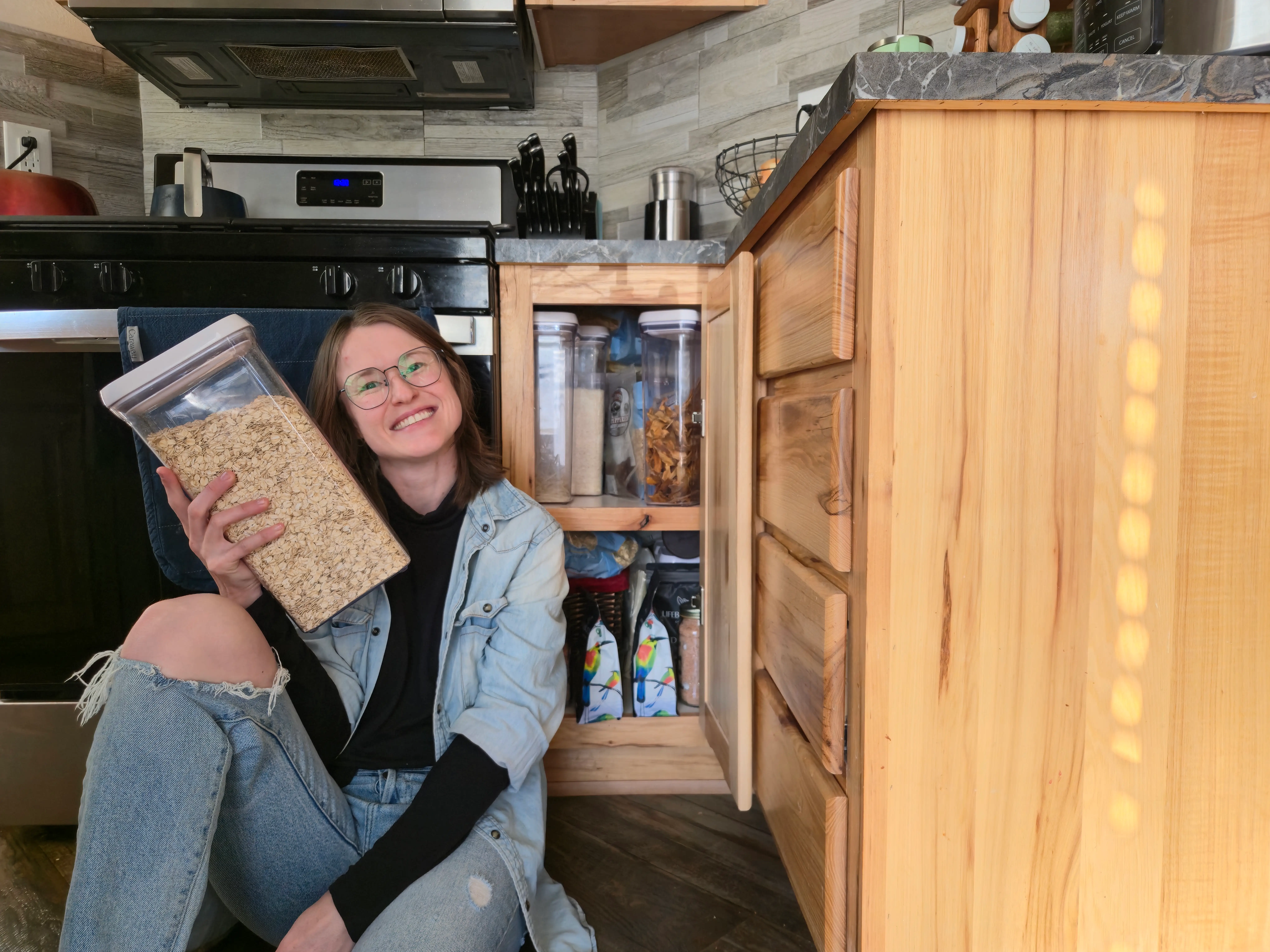 Author Amber McDaniel smiling, holding a bin of dried goods next to open cabinet with bins of dry good inside
