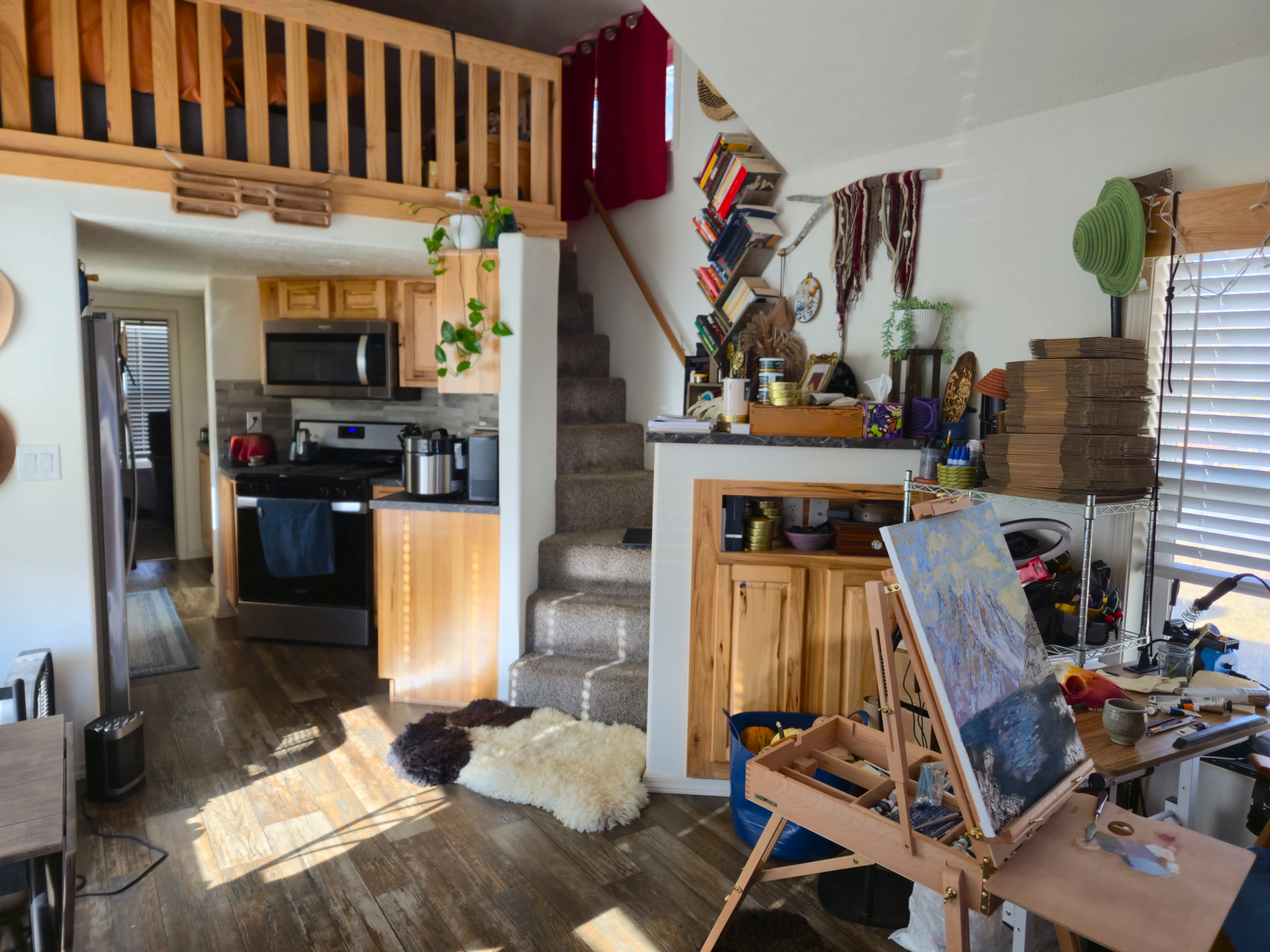Overview of entryway of tiny home with artwork in one corner, staircase, and kitchen area