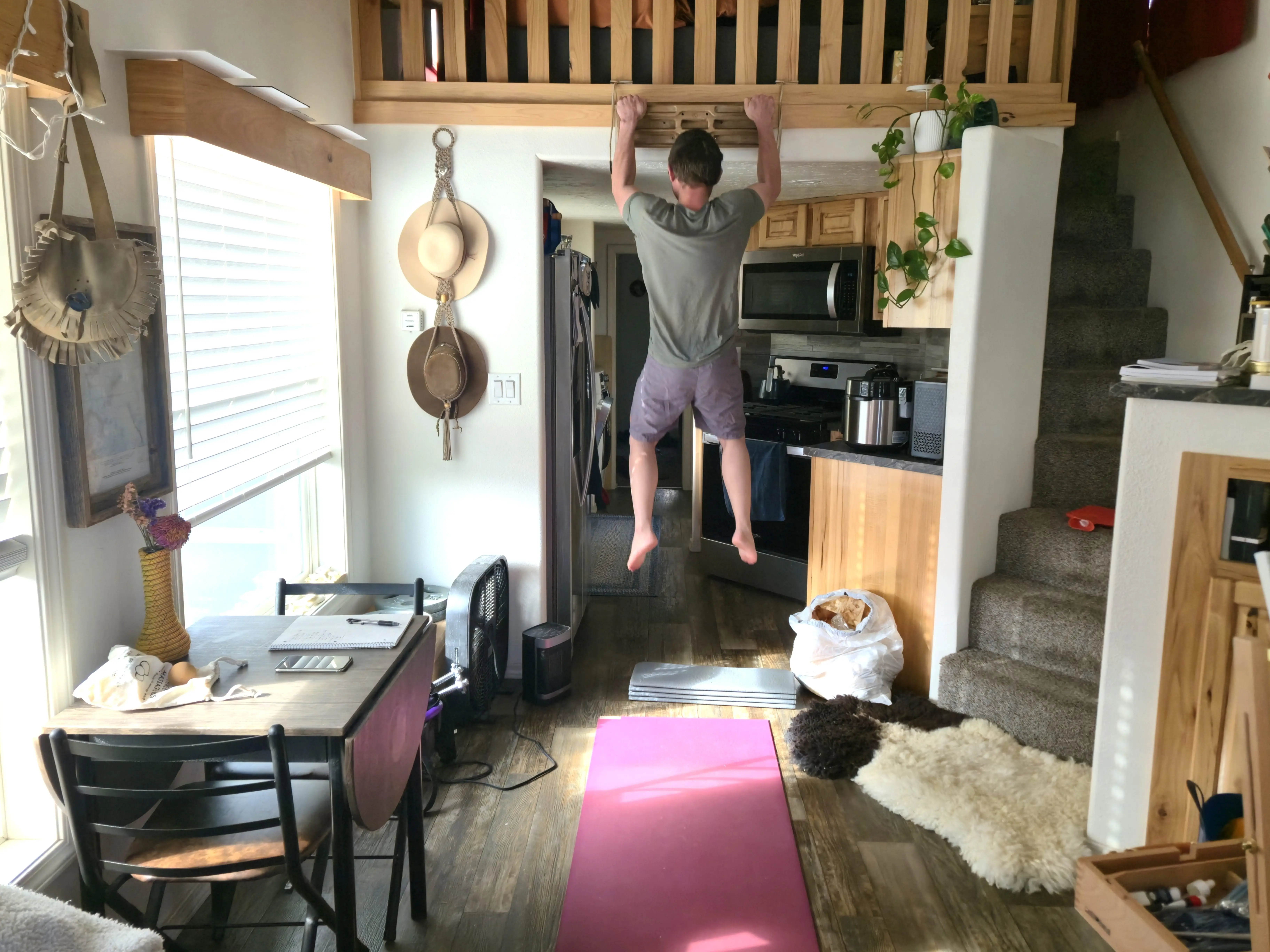 Man holding himself up above a door frame in tiny home with staircase next to him