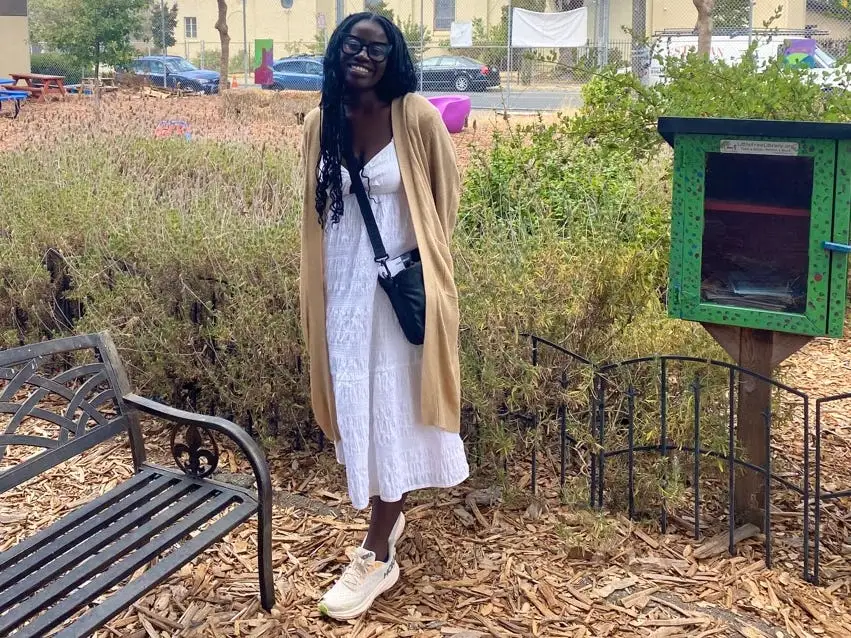 Author Alicia Simba smiling in park next to little free library, bench