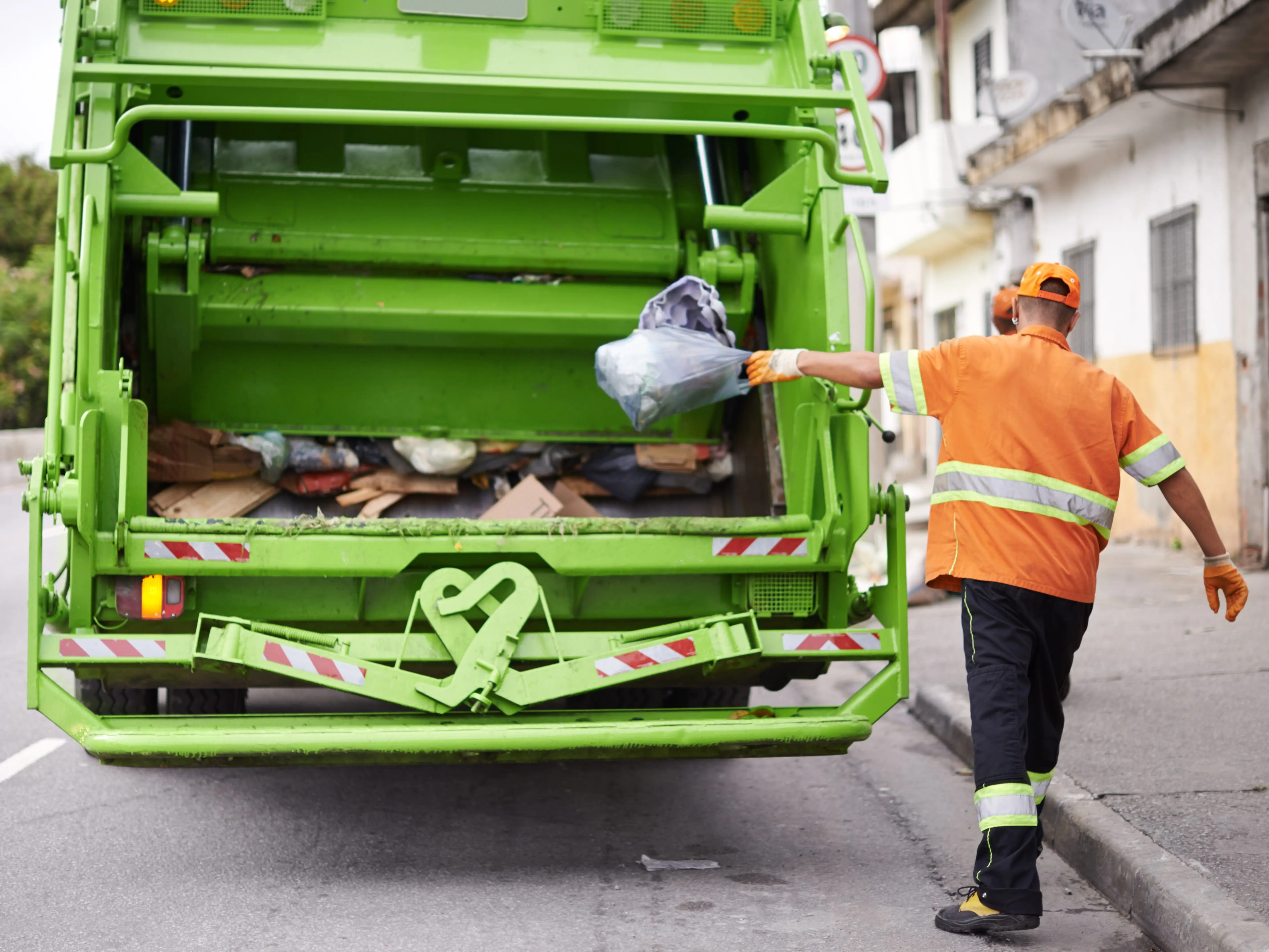 A man throwing recyclables into a truck.