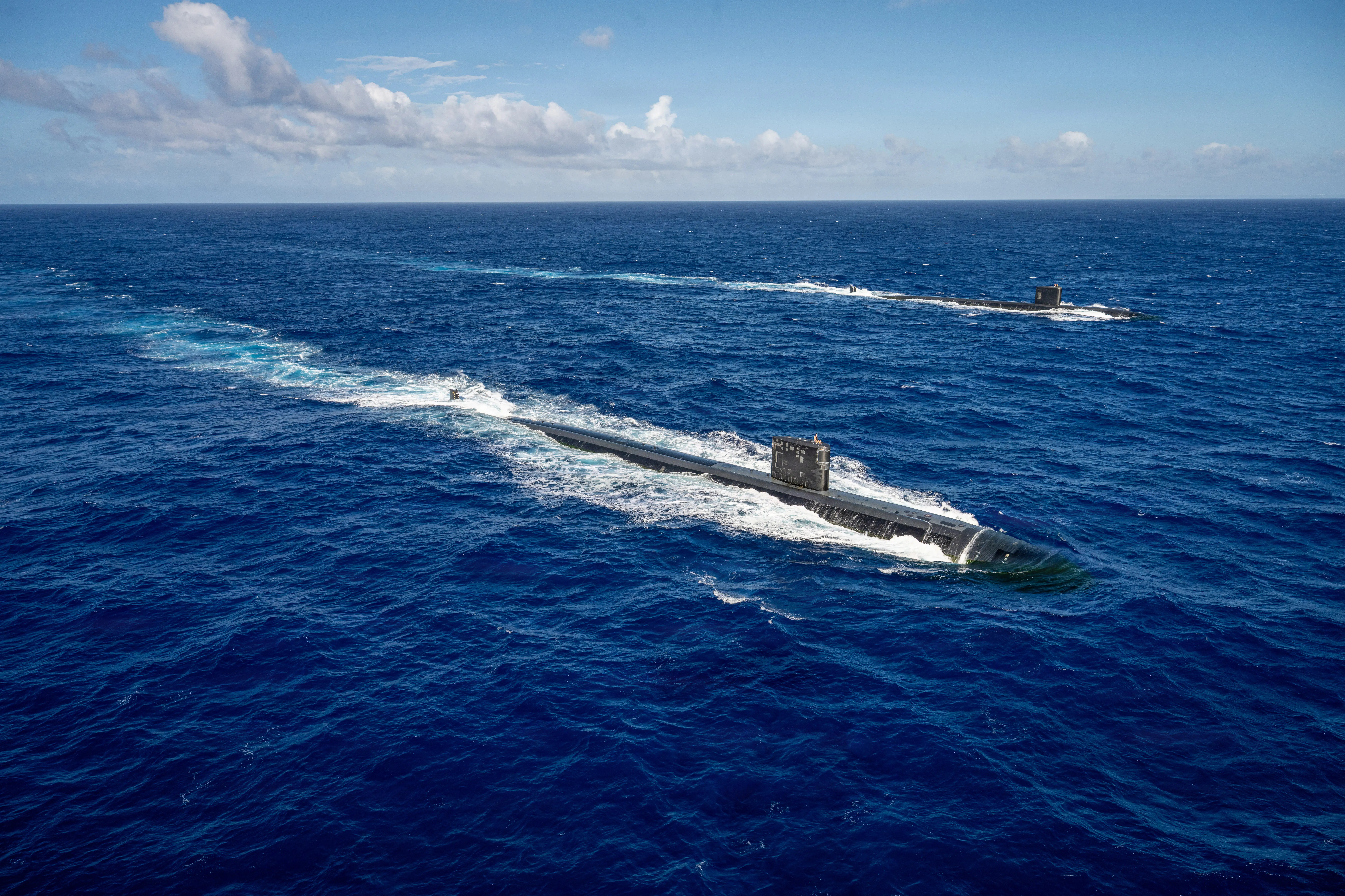 Two US Navy submarines sail in dark blue waters.