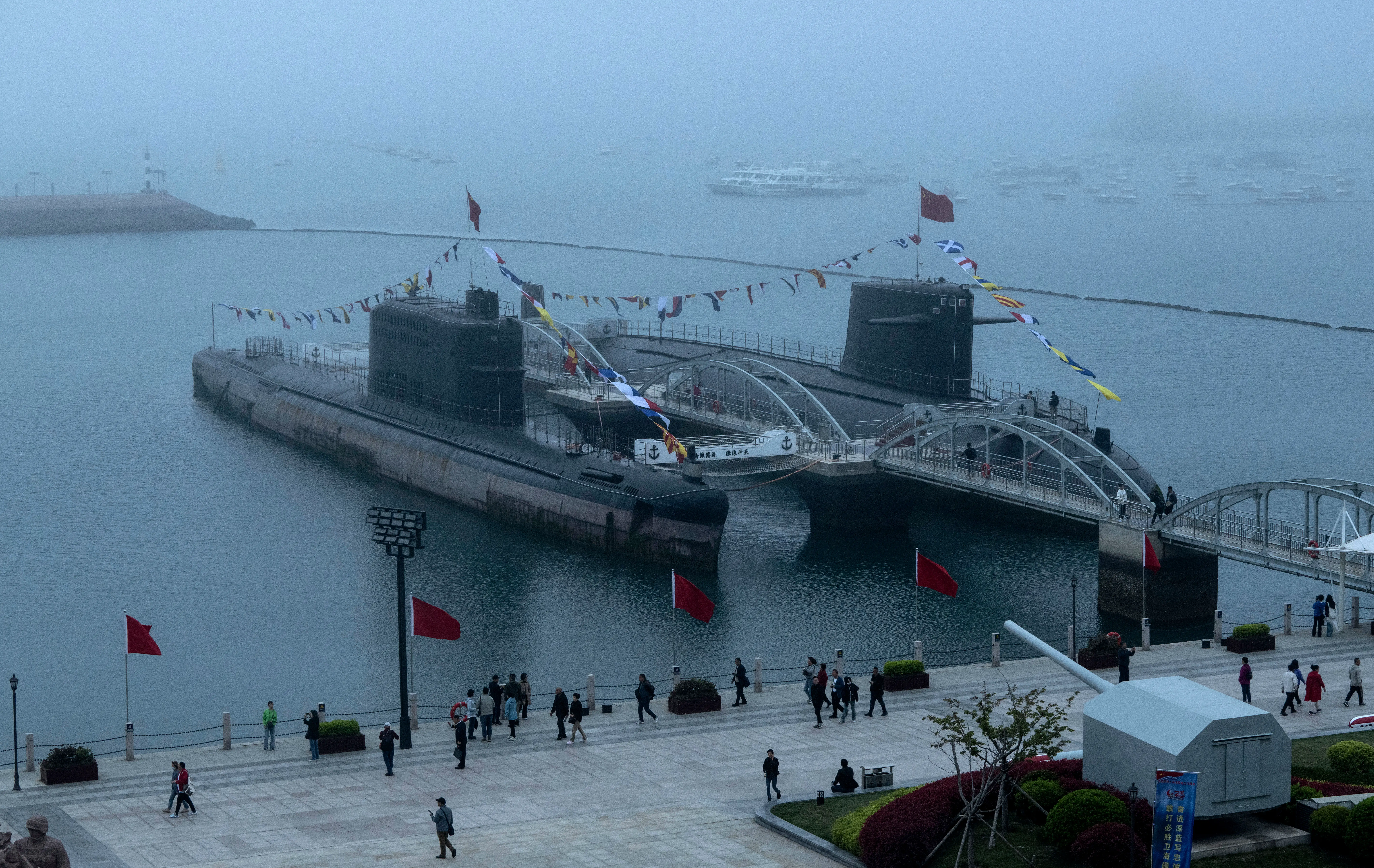 Two Chinese submarines sit in water at a pier.