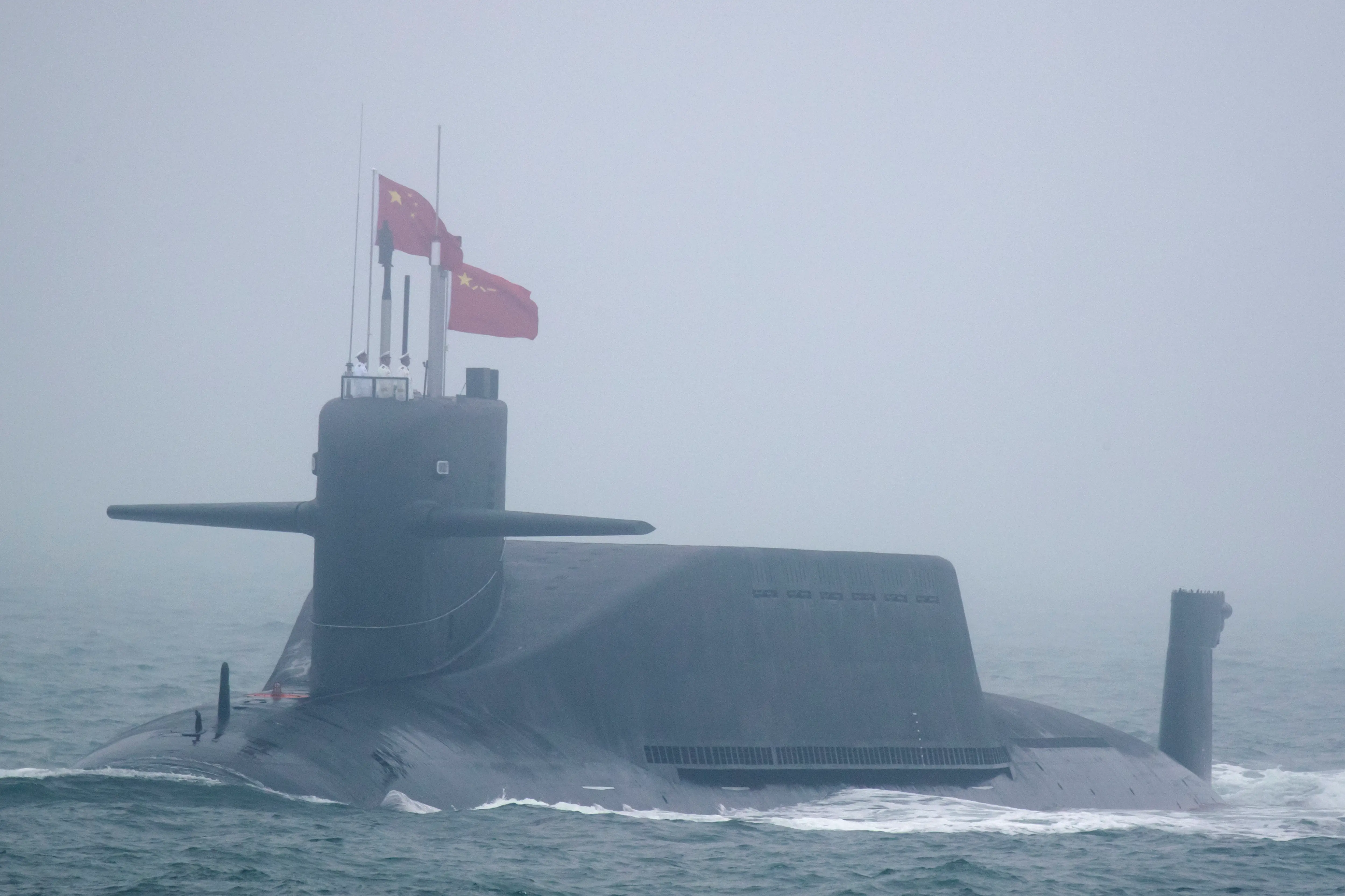 A Chinese submarine sails in the ocean with overcast weather in the background.