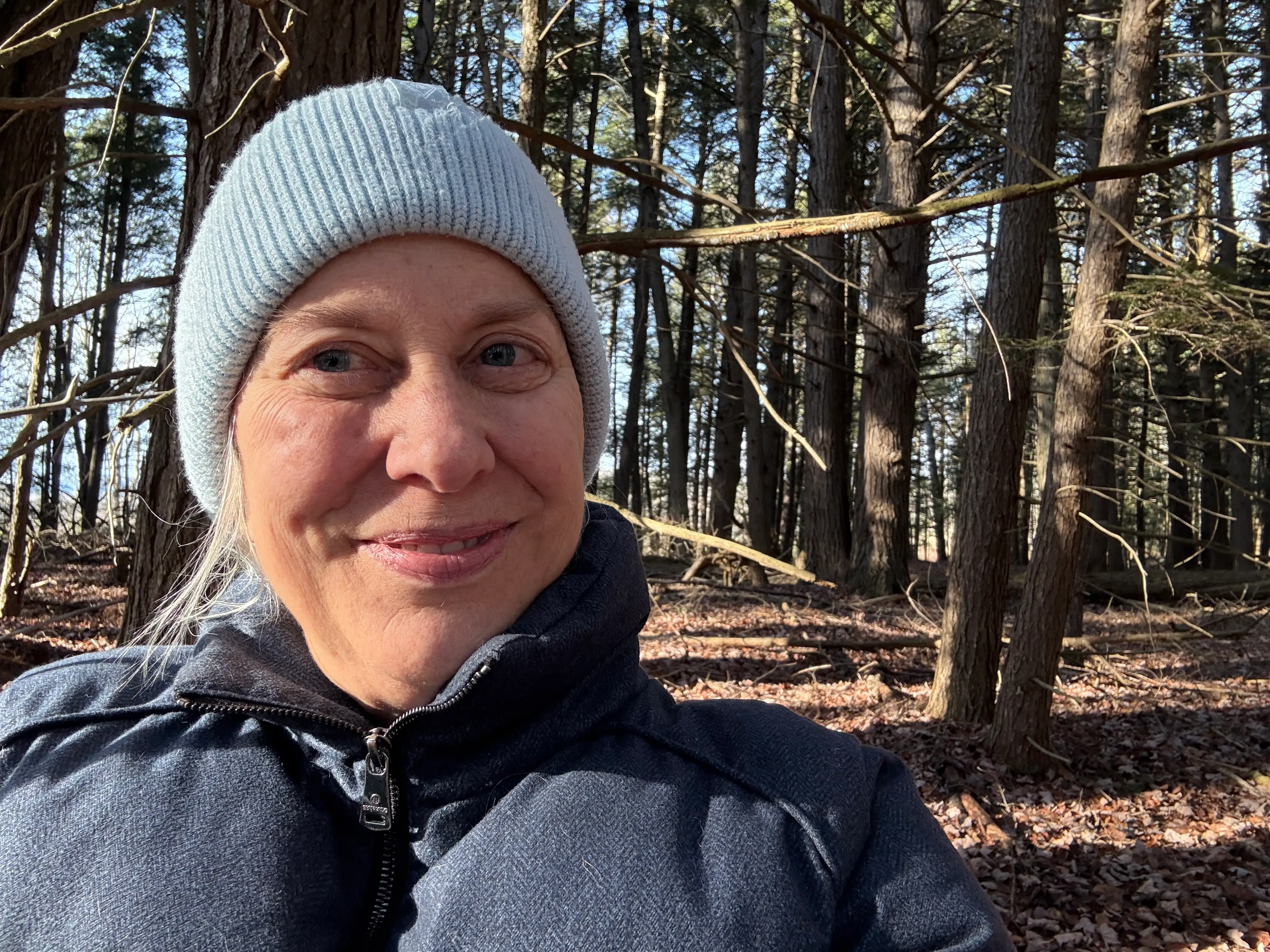 Woman with hat and jacket on smiling amid trees