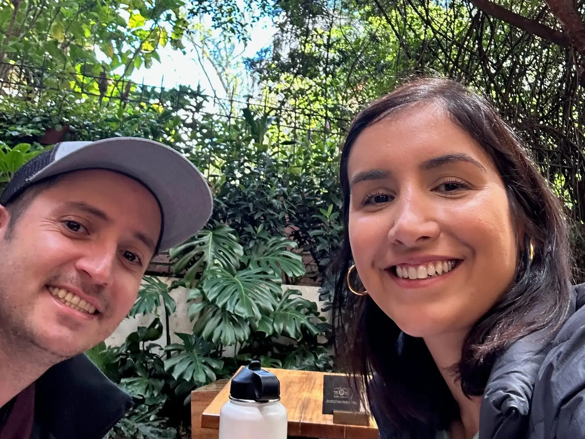 A man and a woman take a selfie at a restaurant, surrounded by trees.