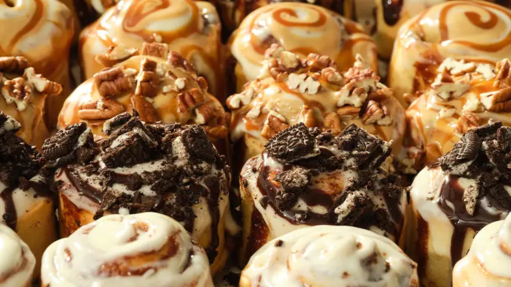 A row of Cinnabon cinnamon rolls with toppings including pecans and Oreo cookies.