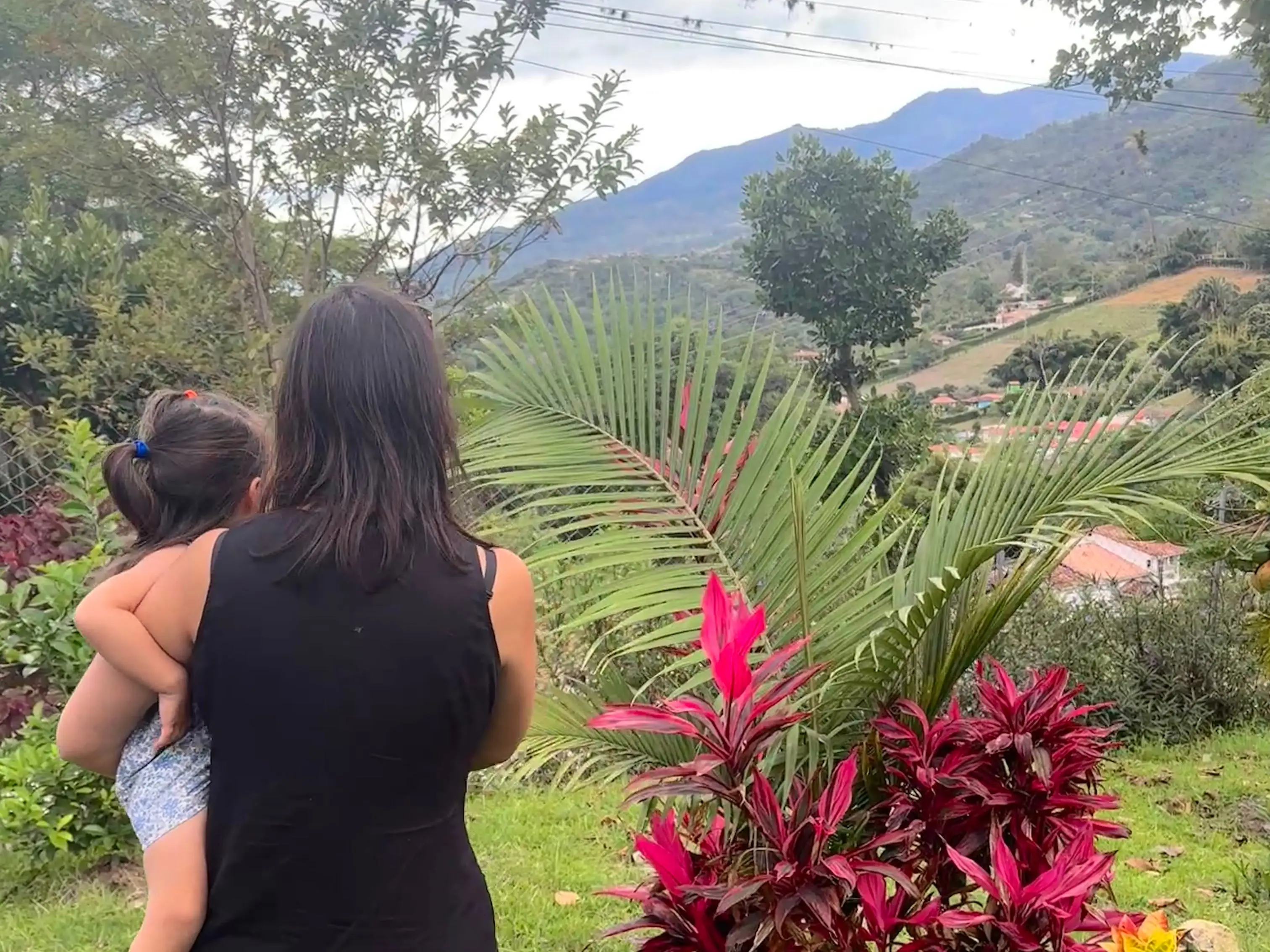 A woman and a young girl look out at a valley of homes, surrounded by trees.