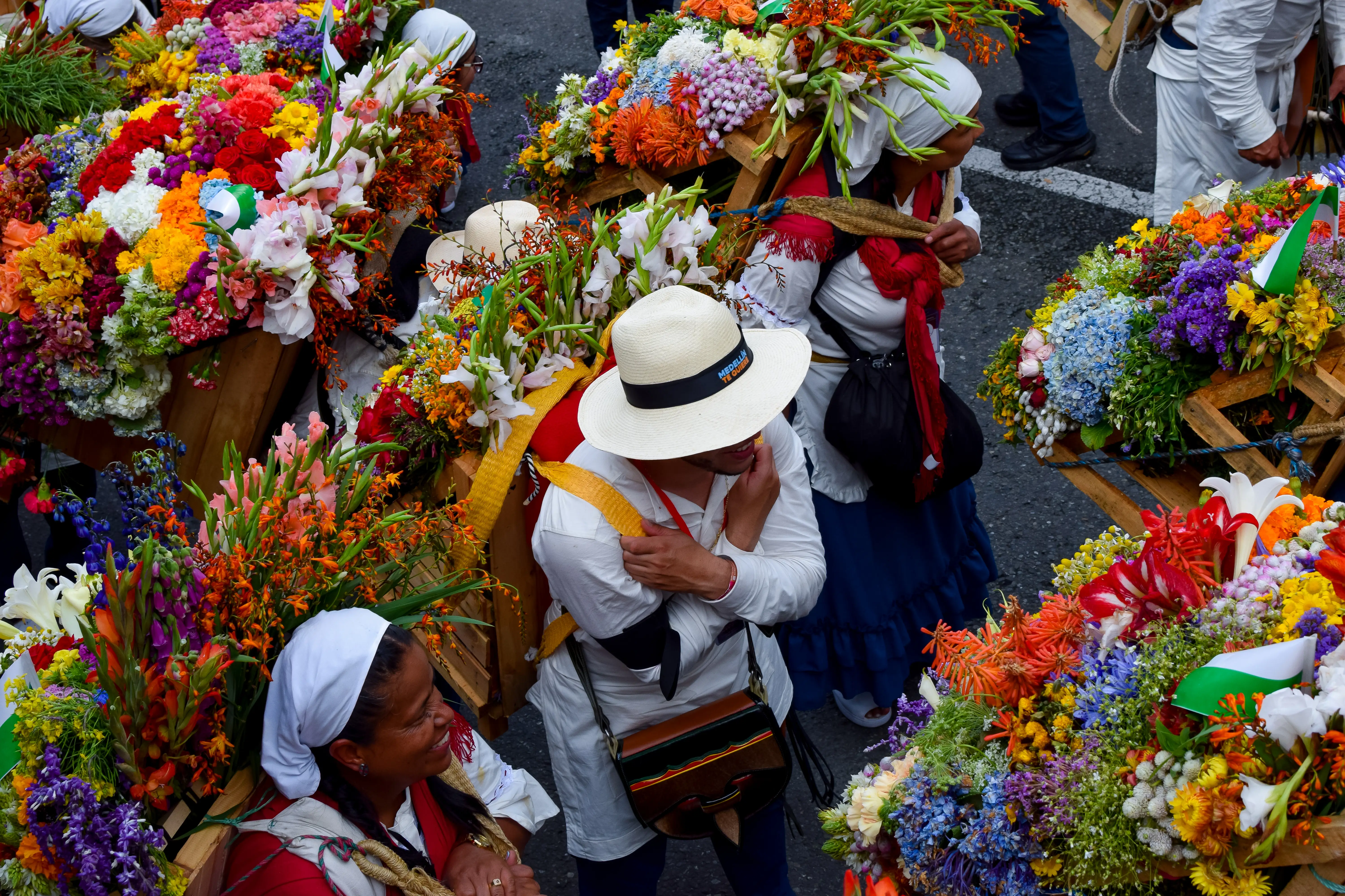 Two women and a man carry bouquets of flowers on their backs.