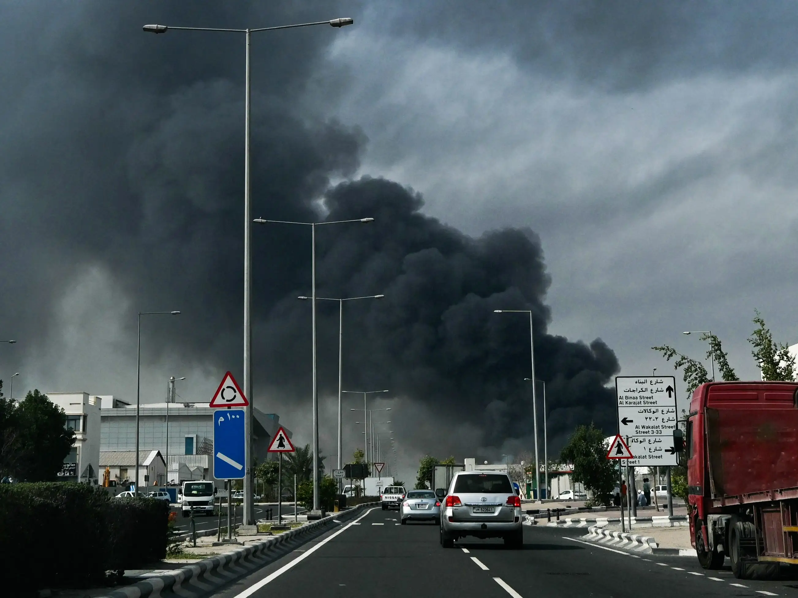 Motorists drive past a plume of smoke rising from a reported Iranian strike in the industrial district of Doha on March 1, 2026