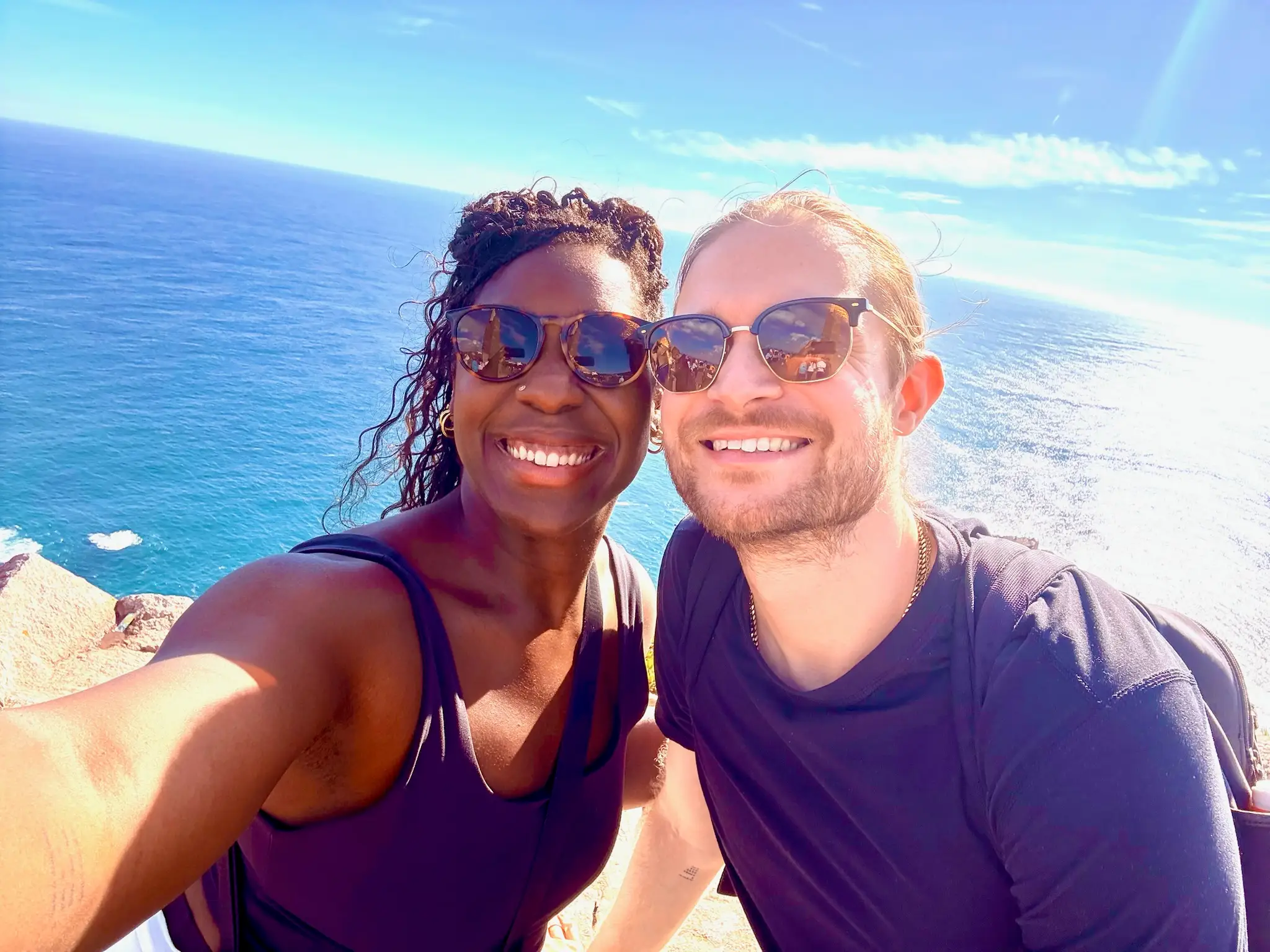 Two people in sunglasses smiling in front of water