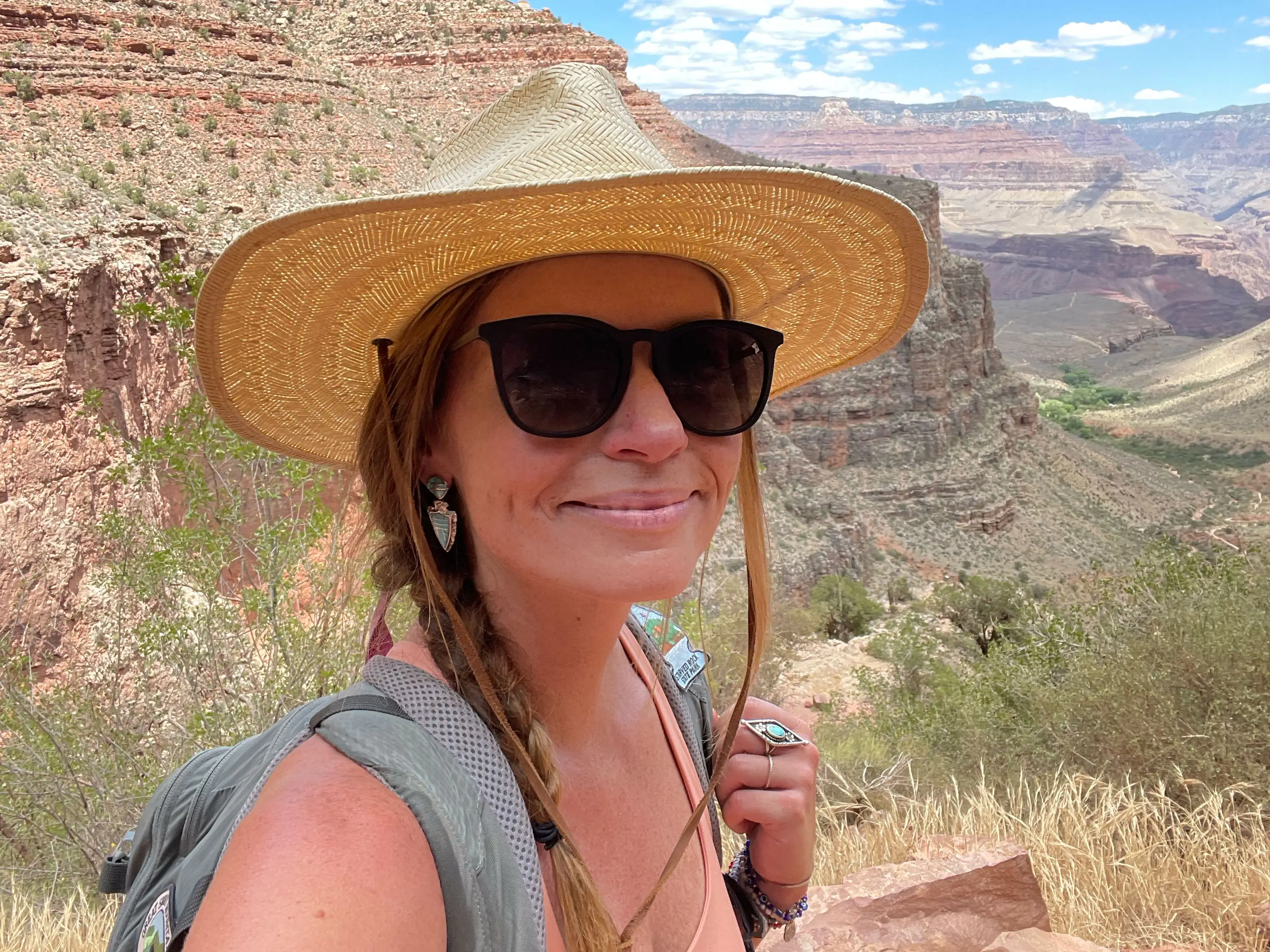 Emily, wearing a sun hat, sunglasses, and a backpack, poses for a photo at the Grand Canyon.