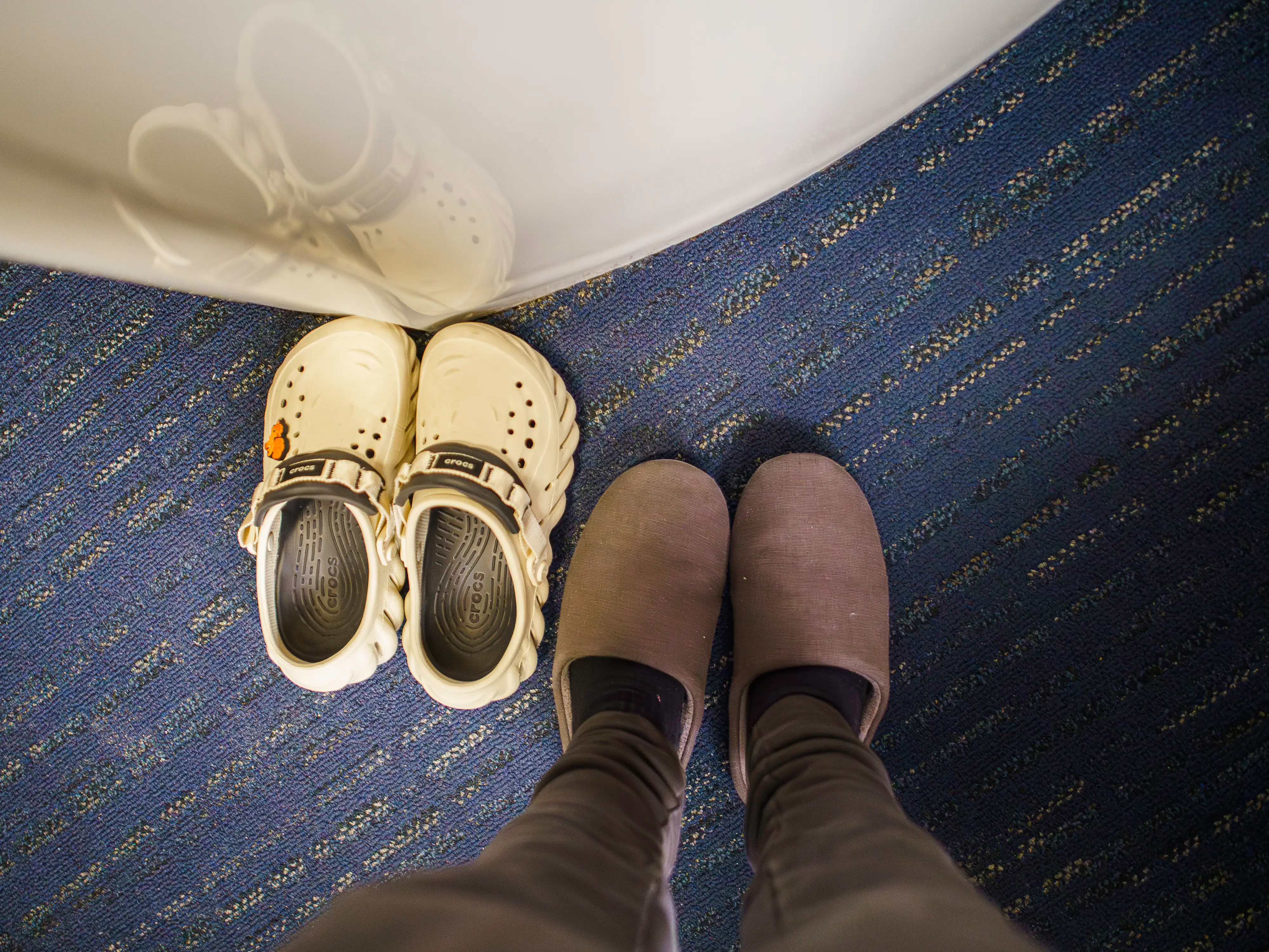 An aerial view of the author's feet in slippers next to a pair of Crocs