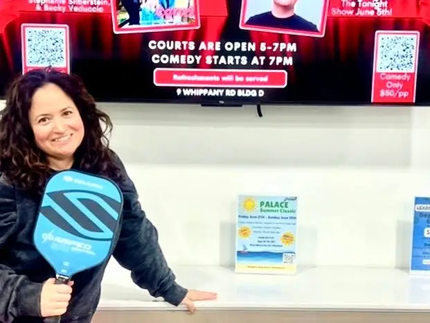 Holly Rizzuto Palker stands in front of a sign promoting her stand-up comedy show.
