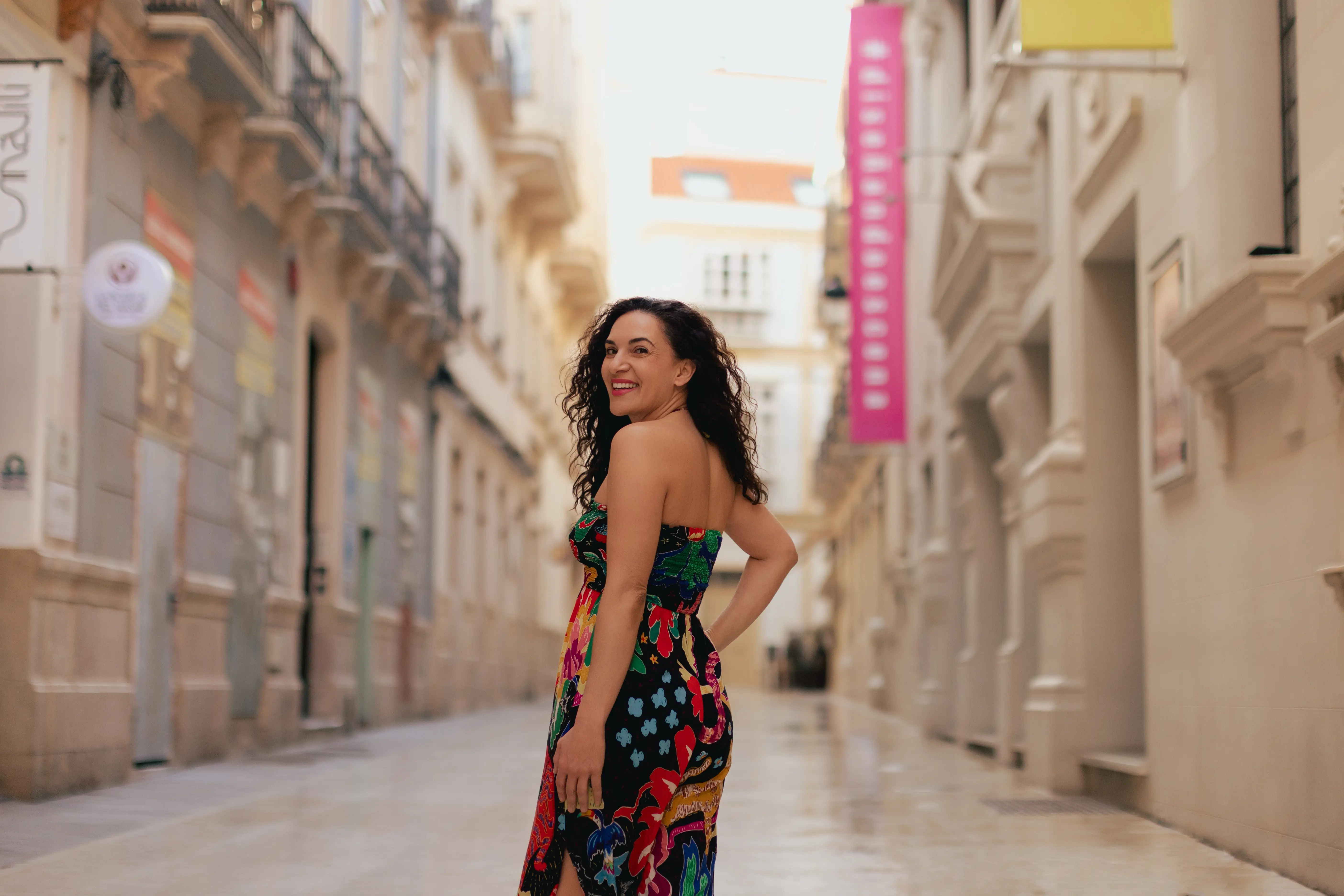 Author Cepee Tabibian smiling over shoulder in middle of walkway between buildings