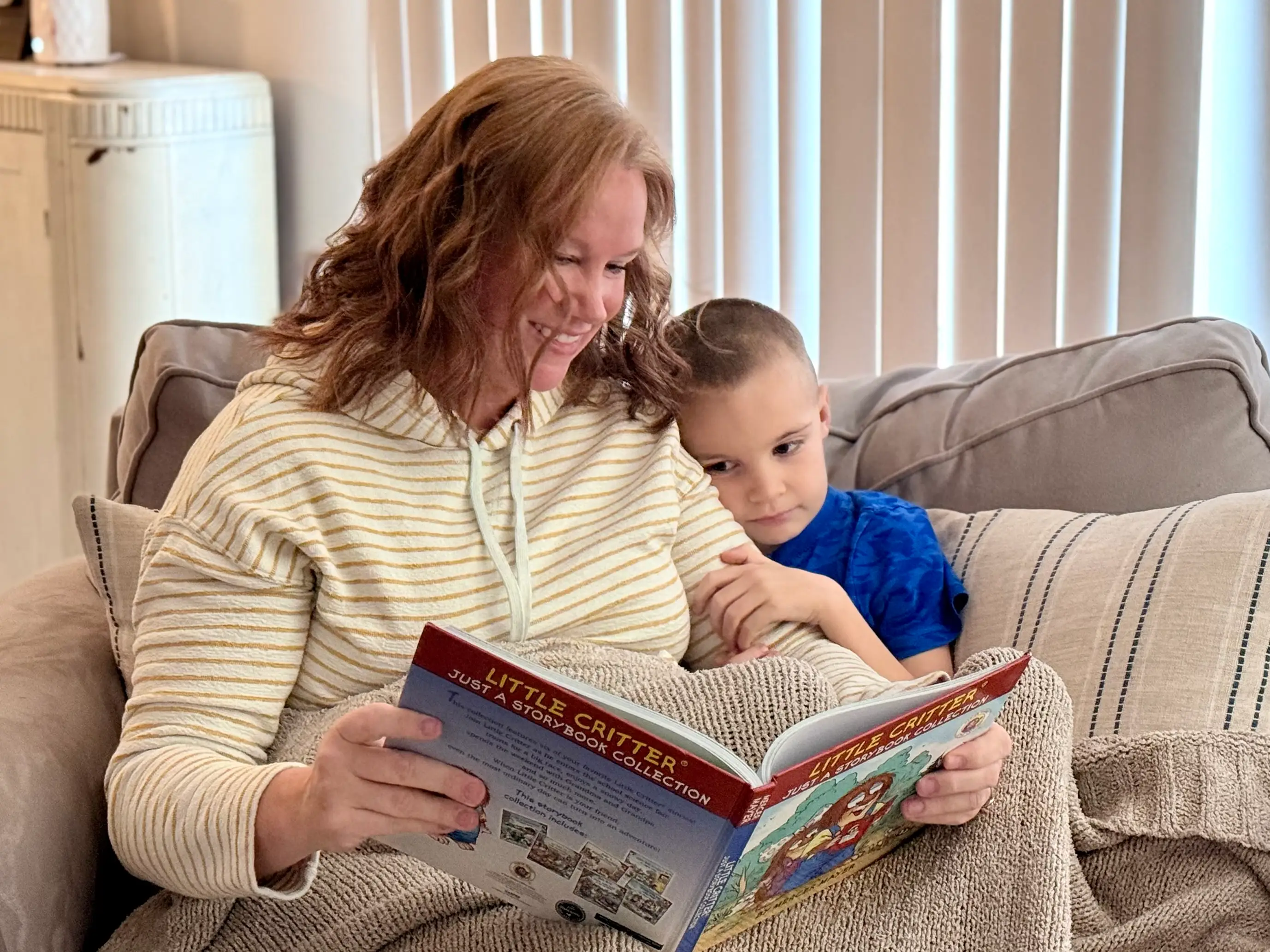 The author reads to her young son on a couch.