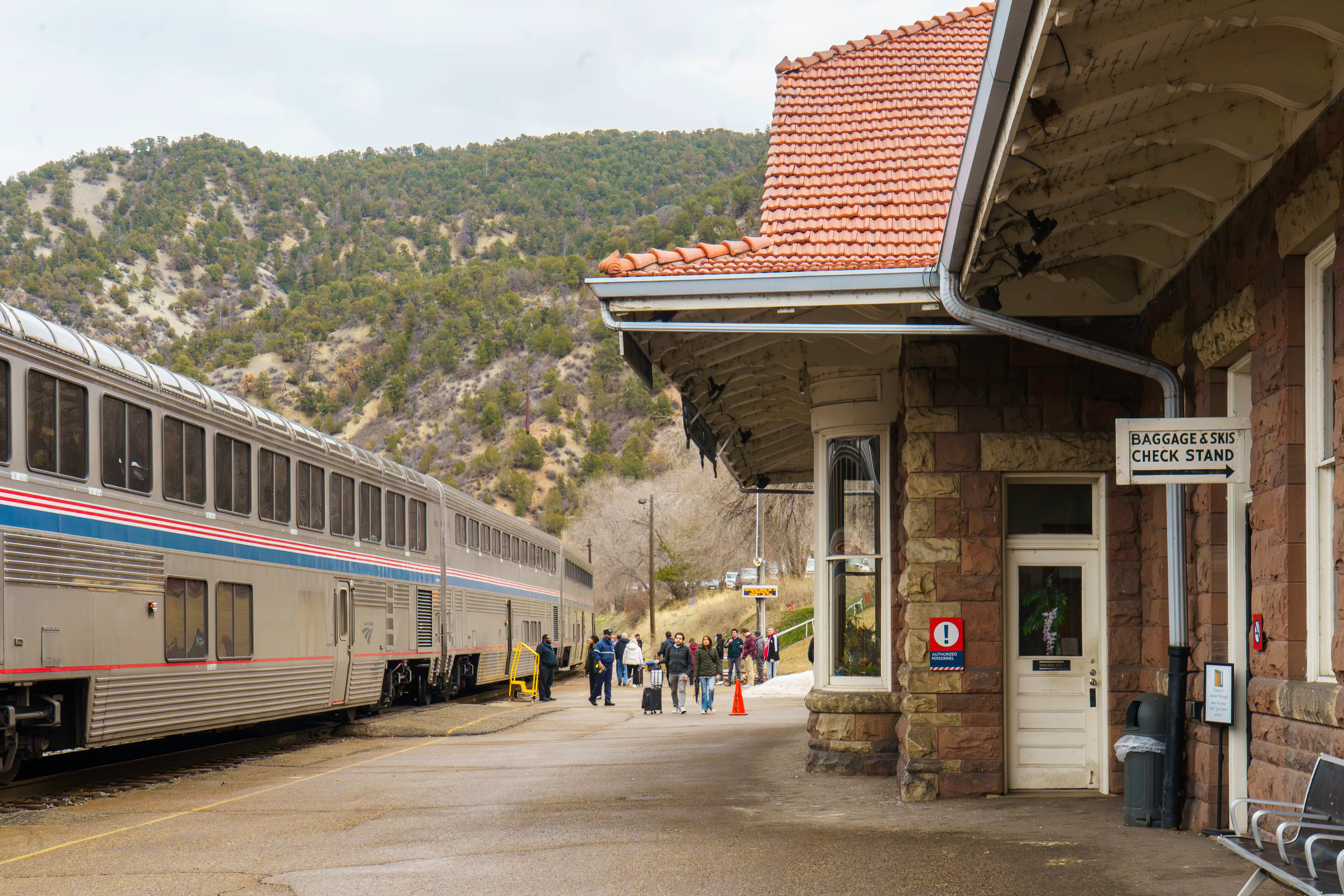 A train stopped on the left with a station on the right and a mountan behind