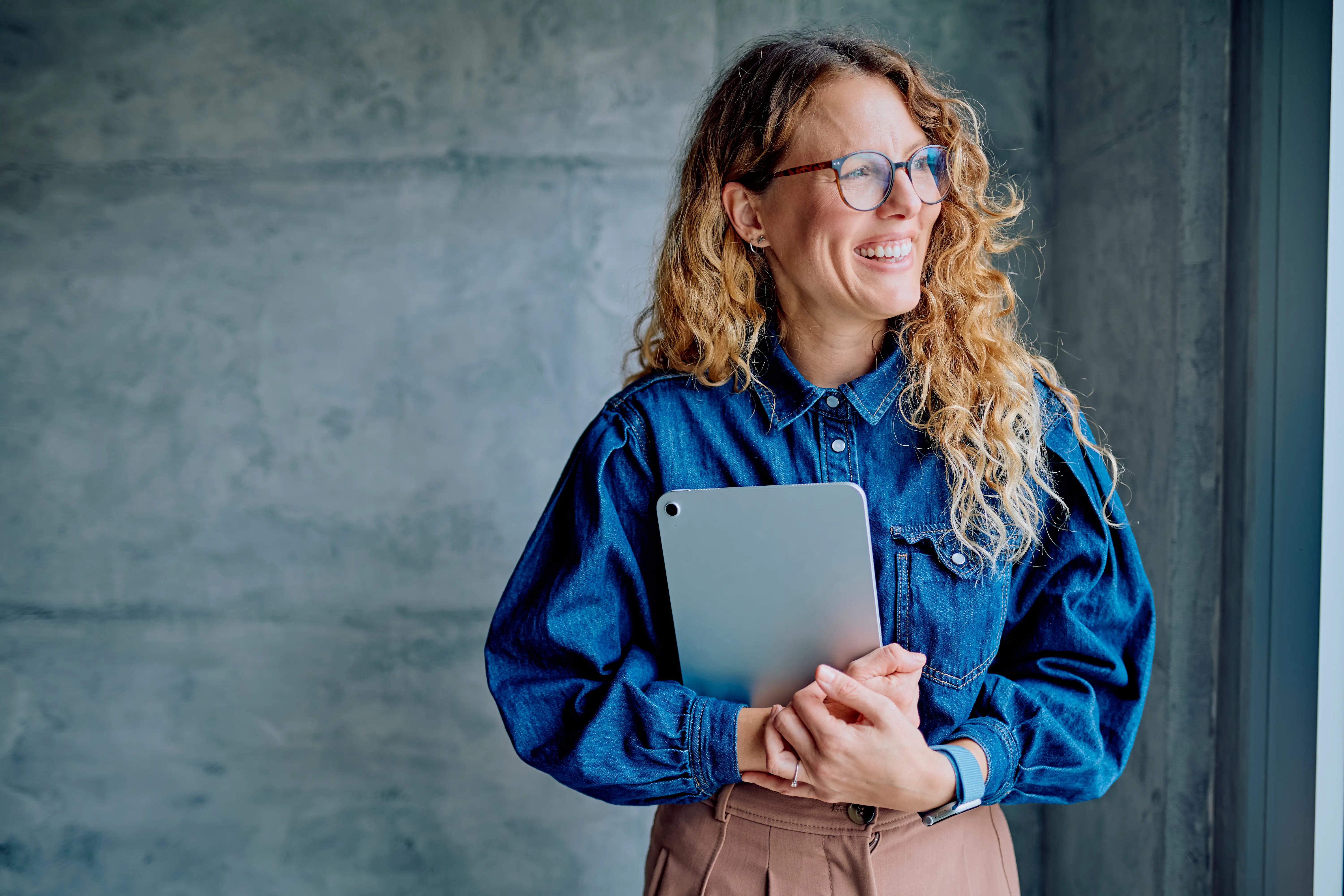 A woman wearing a denim shirt holding an iPad.