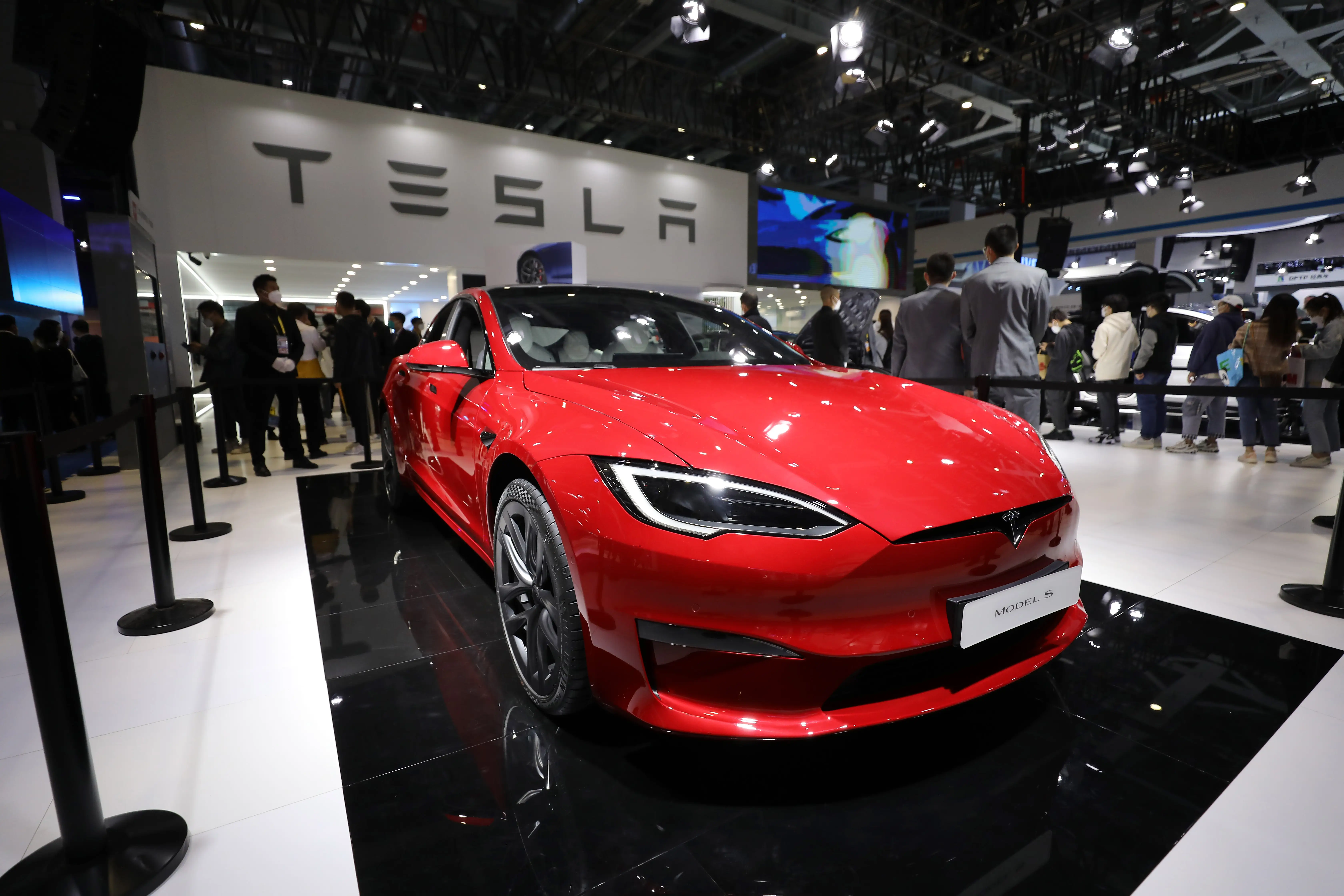 A red Tesla Model S is parked on black tile during a car show.