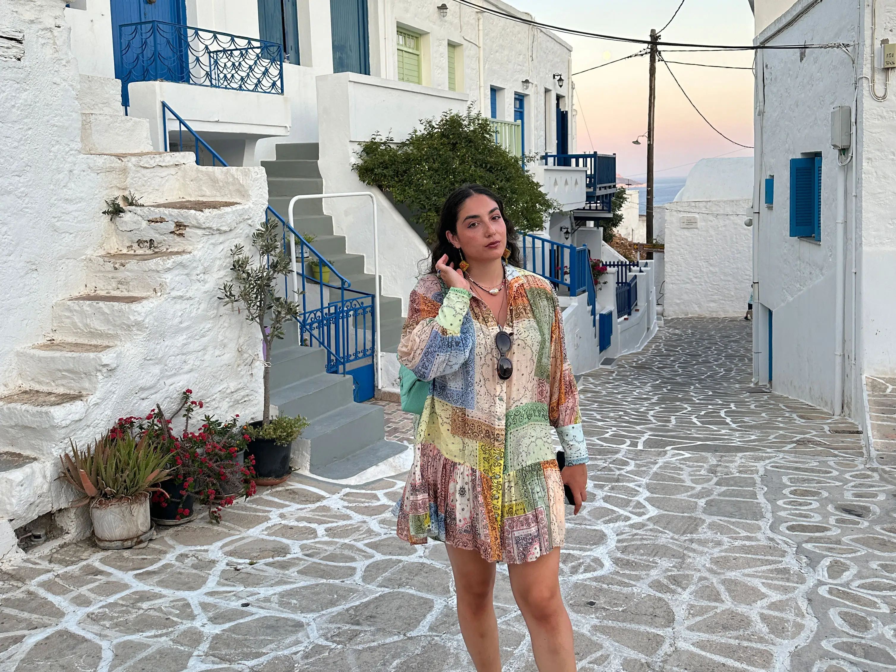 Fani poses in a cobblestone alley lined with blue and white buildings at sunset.
