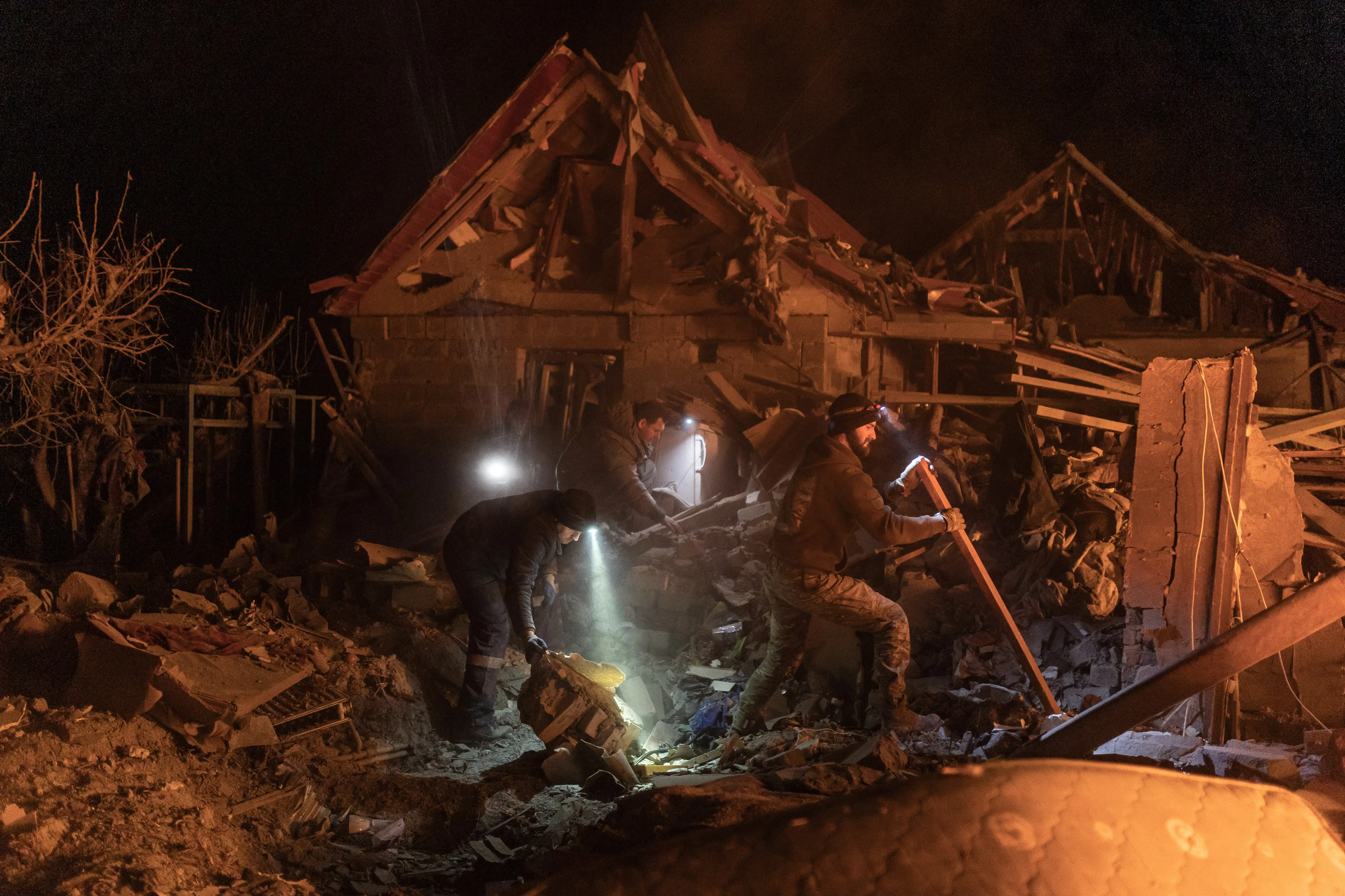 A ruined house at night, with people in head torches searching outside