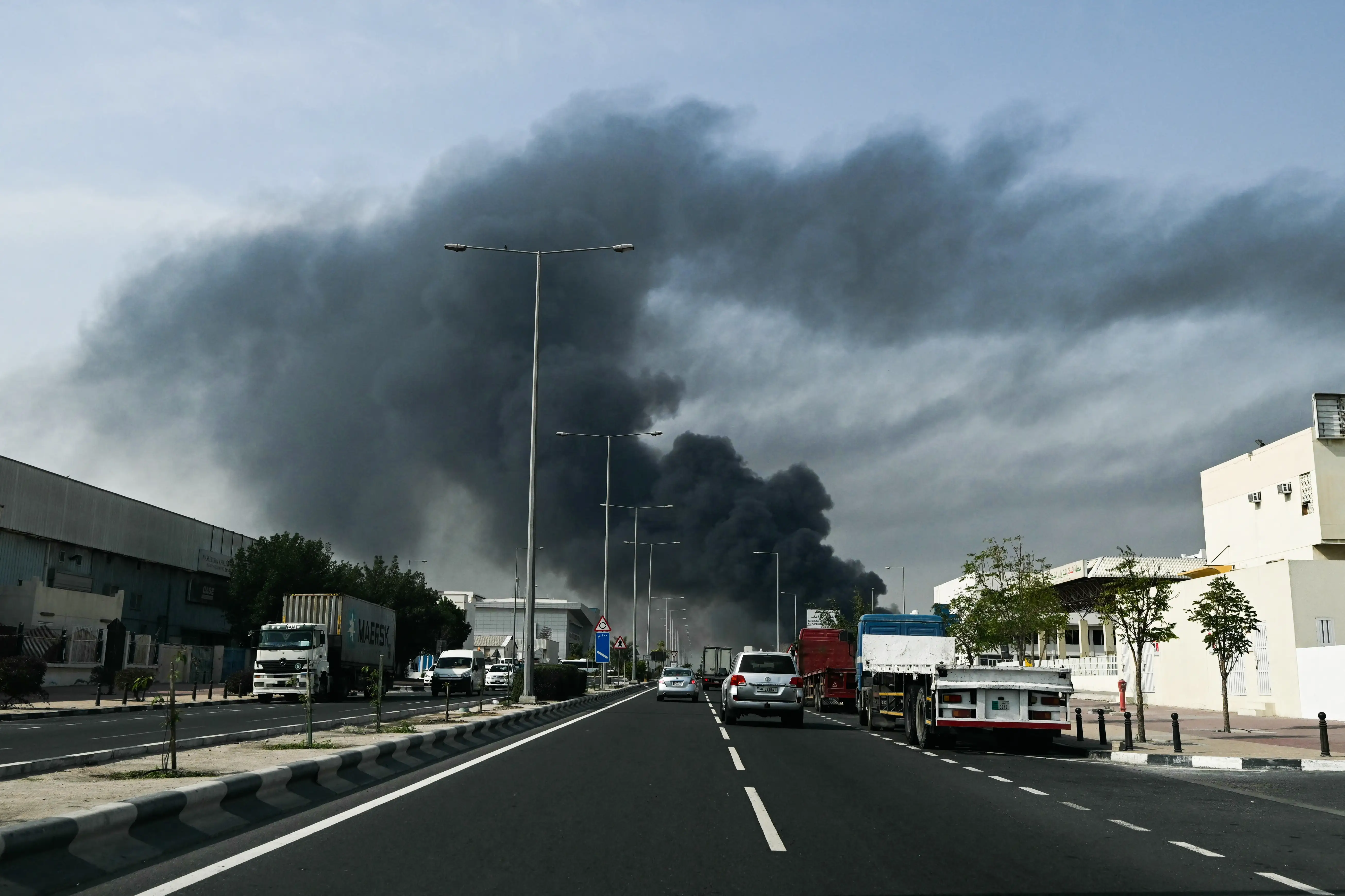 Black smoke rises into a blue sky, with a black tarmac road in the foreground
