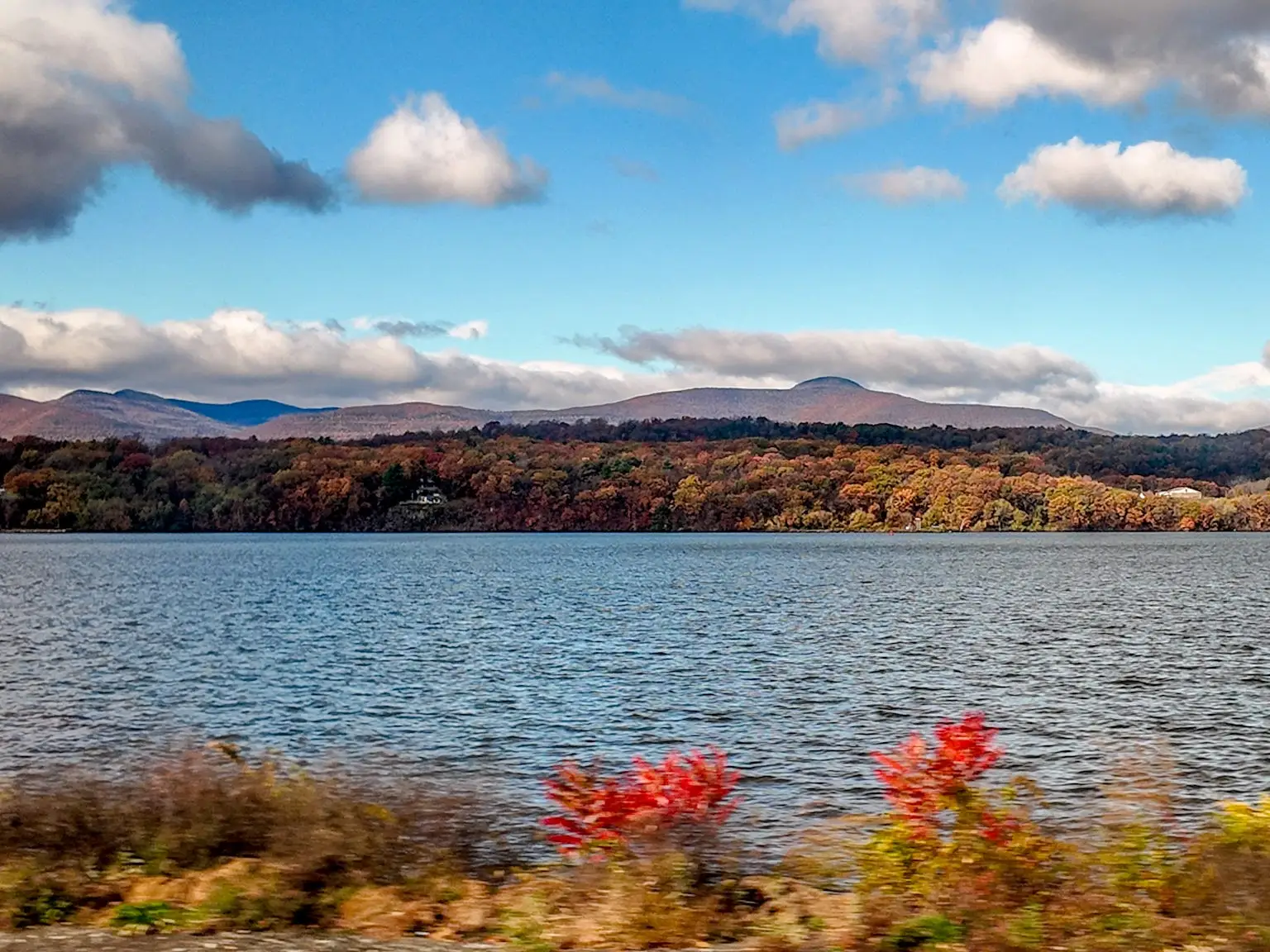 The view out a train window of a river surrounded by fall foliage and mountains.