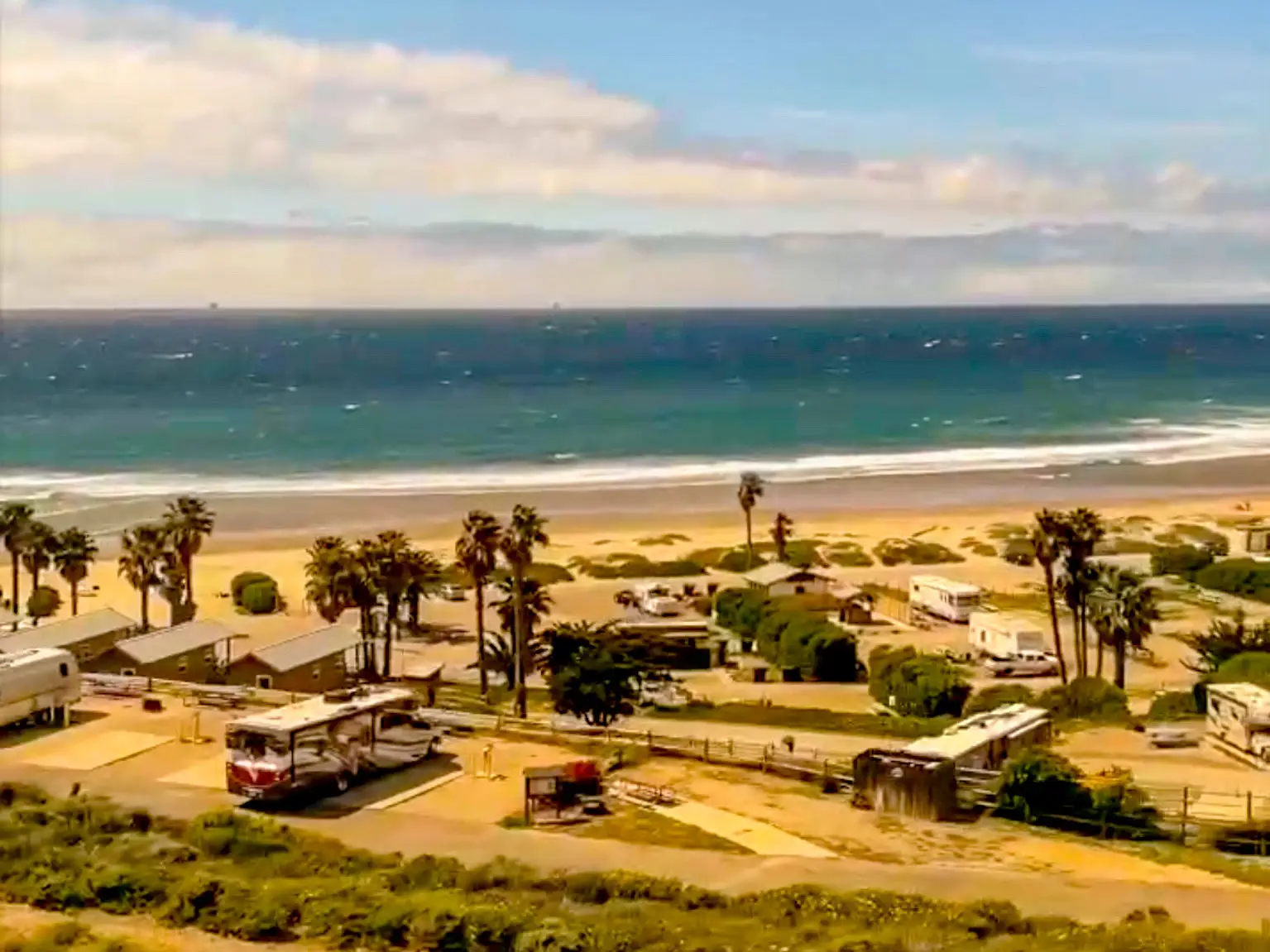 The view out a train window of a beach with palm trees and RVs.