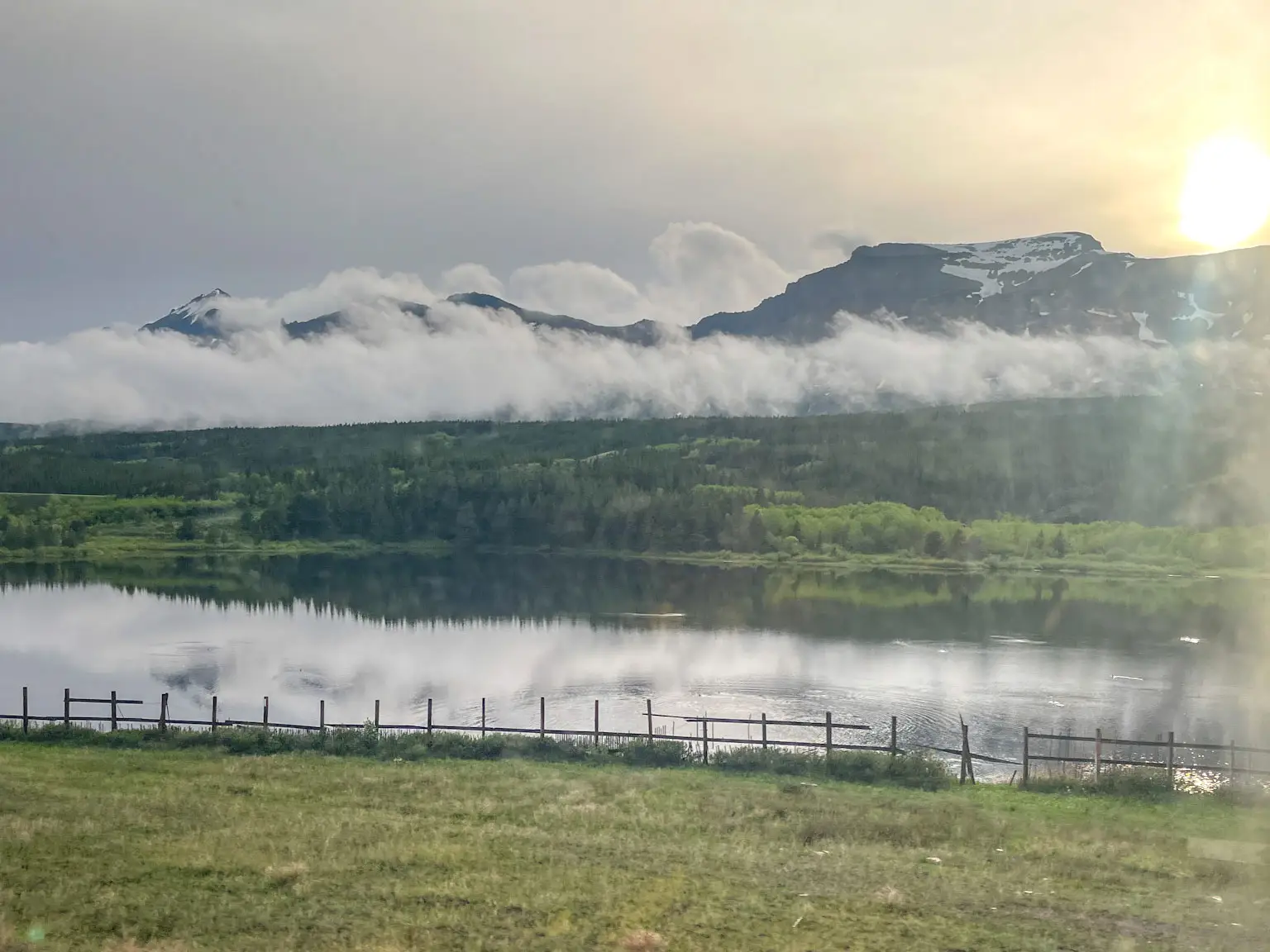 The view out a train window of a cloud-covered mountain and river.