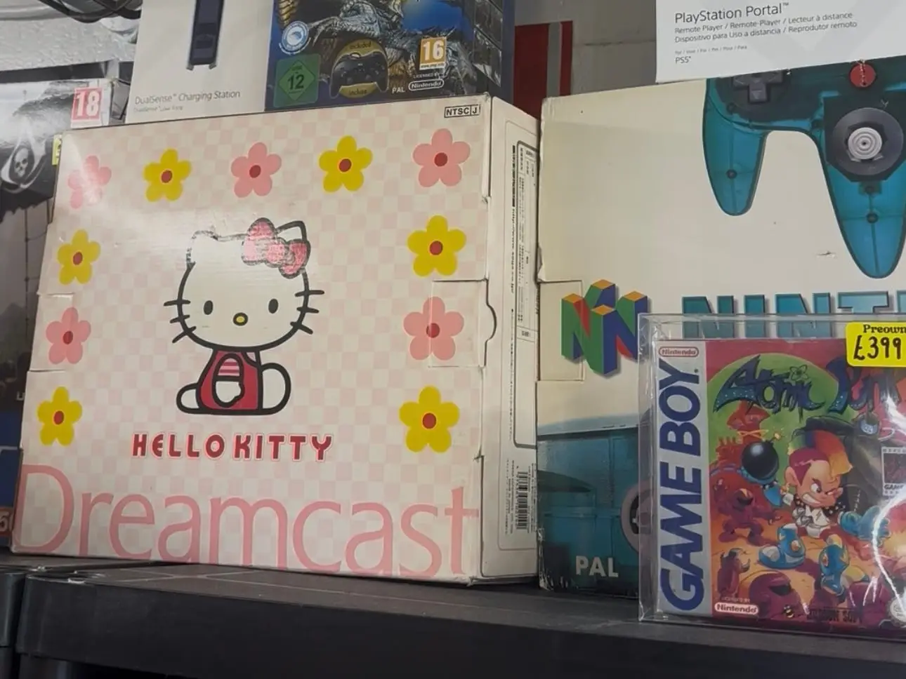 Hello Kitty version of Dreamcast placed on shelf surrounded by other retro games and consoles.