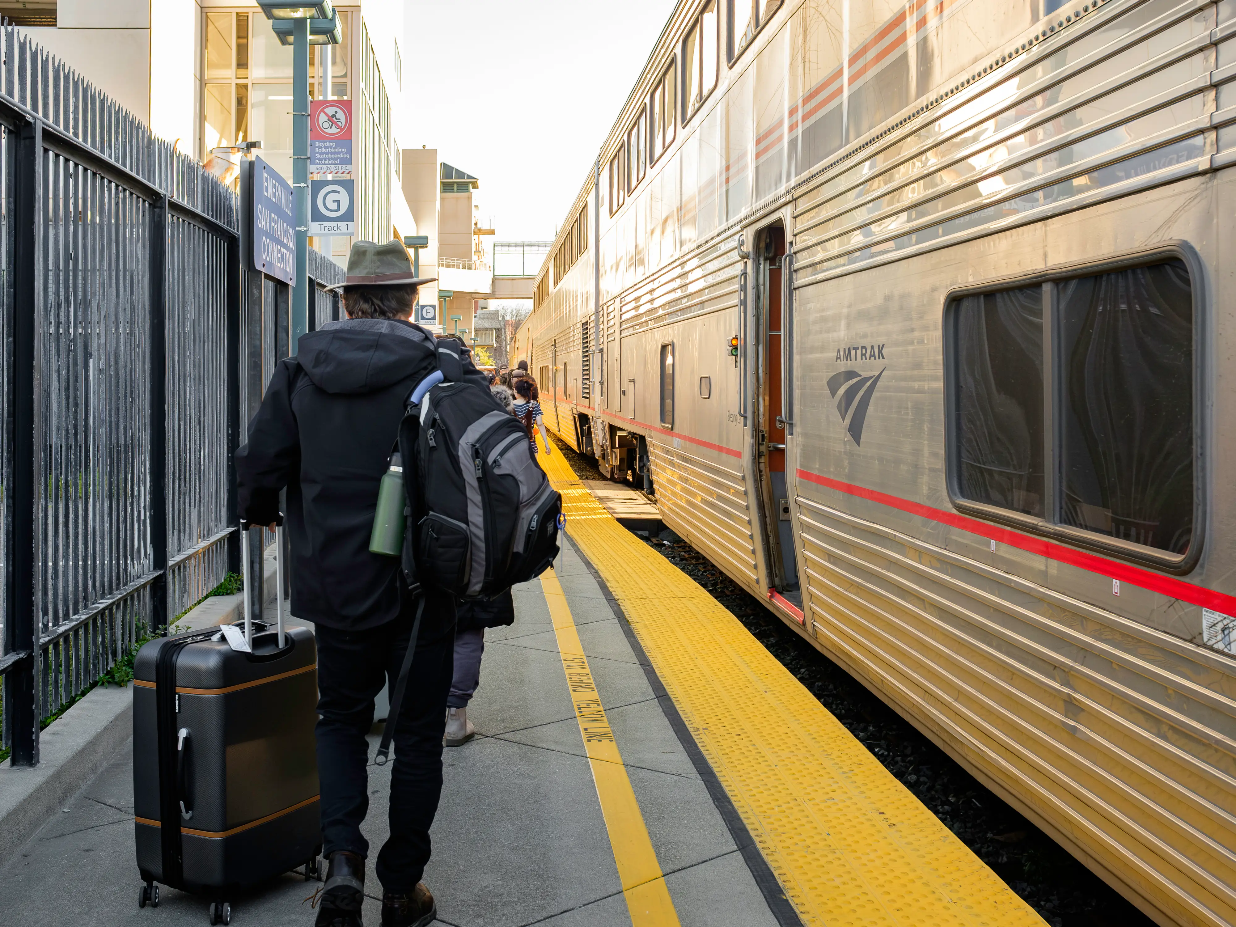 A train stopped at a platform on the right, and people walk with suitcases on the left