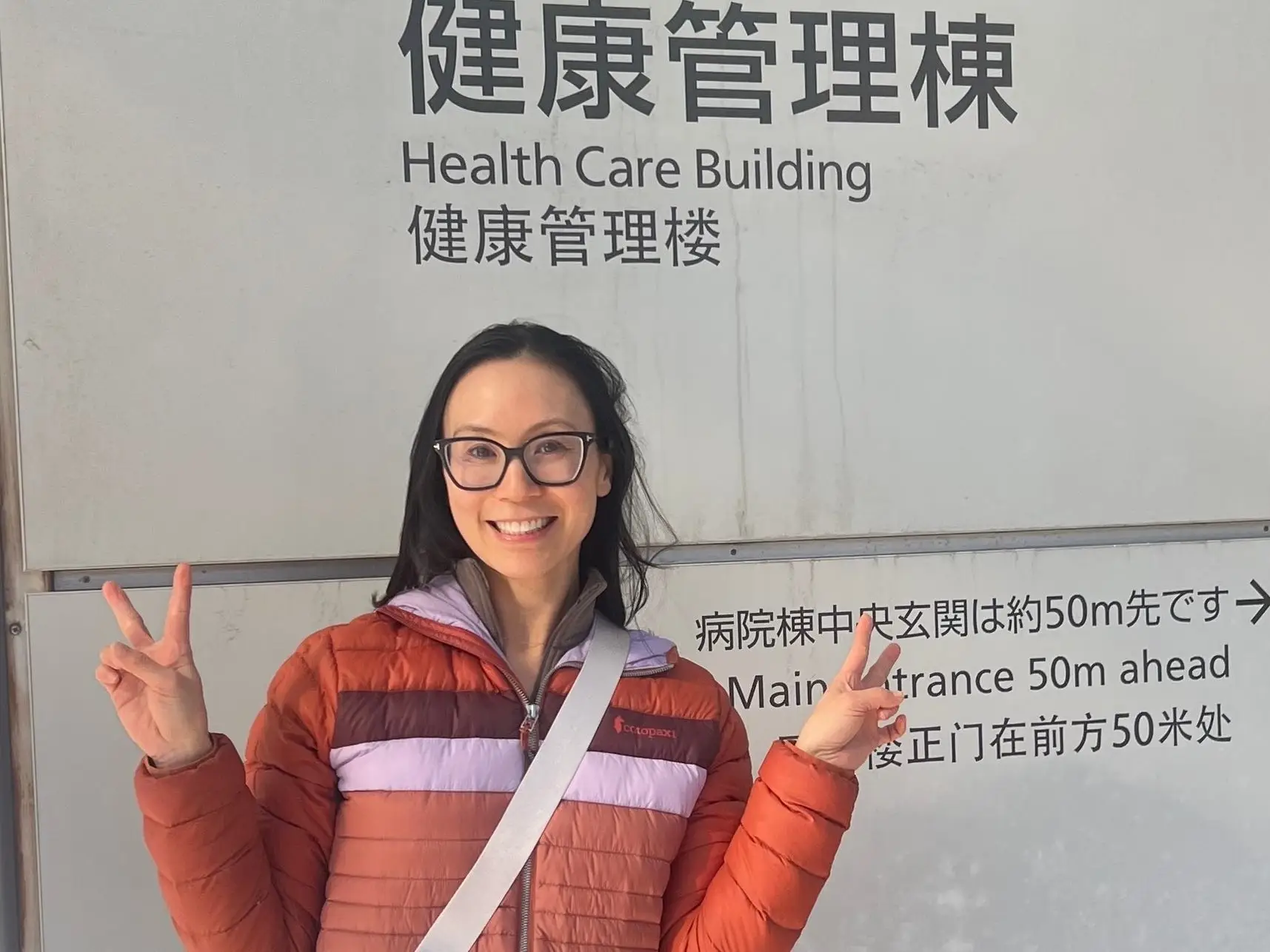 author Ingrid Yang smiling outside of sign for healthcare building In Japan