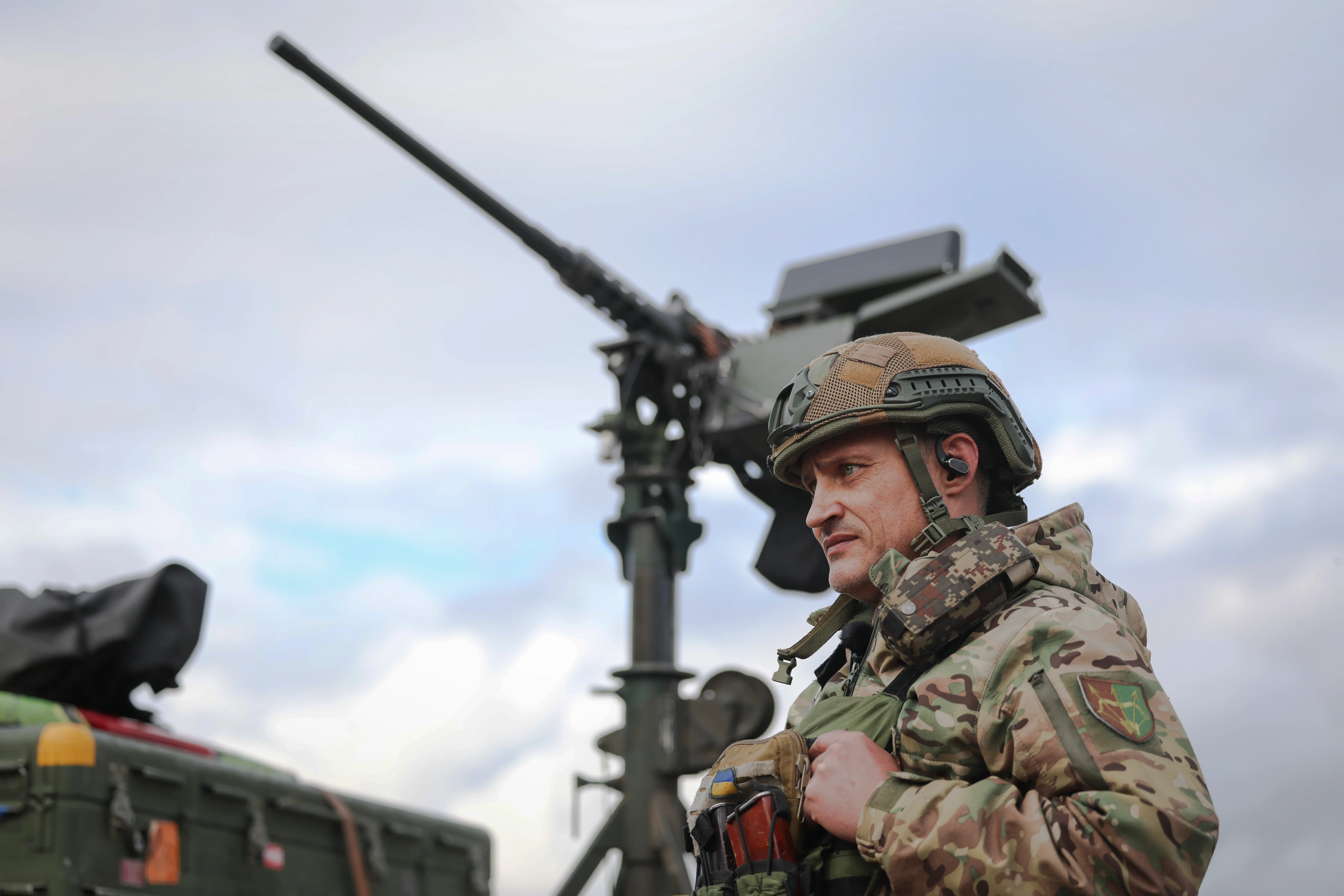 A Ukrainian soldier stands in front of a machine gun turret mounted on the back of a pickup truck.